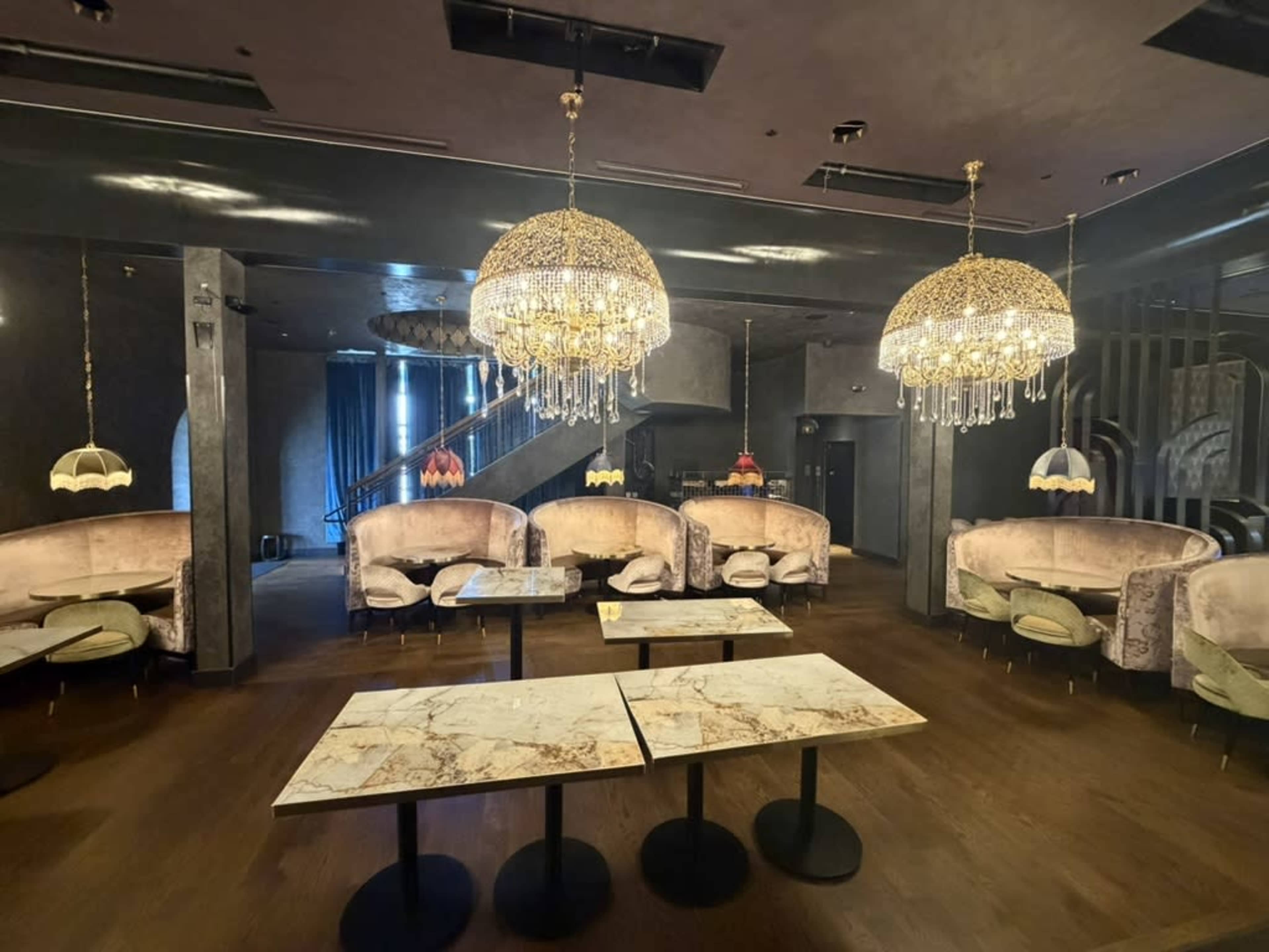 The image shows a dimly lit upscale restaurant interior with plush seating, marble-topped tables, and ornate chandeliers.