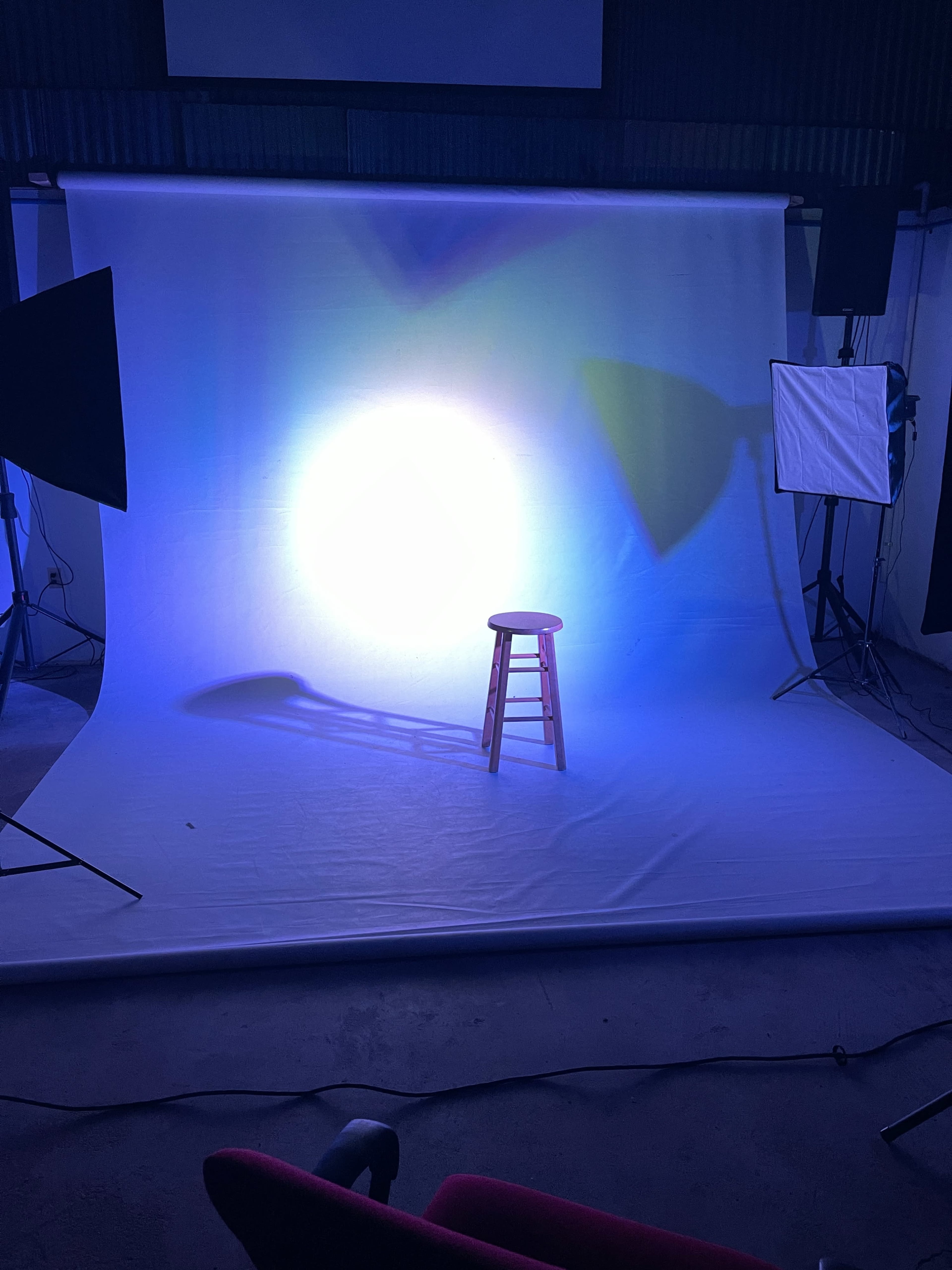 A brightly lit photography set with a wooden stool positioned on a white backdrop, surrounded by studio lighting equipment.