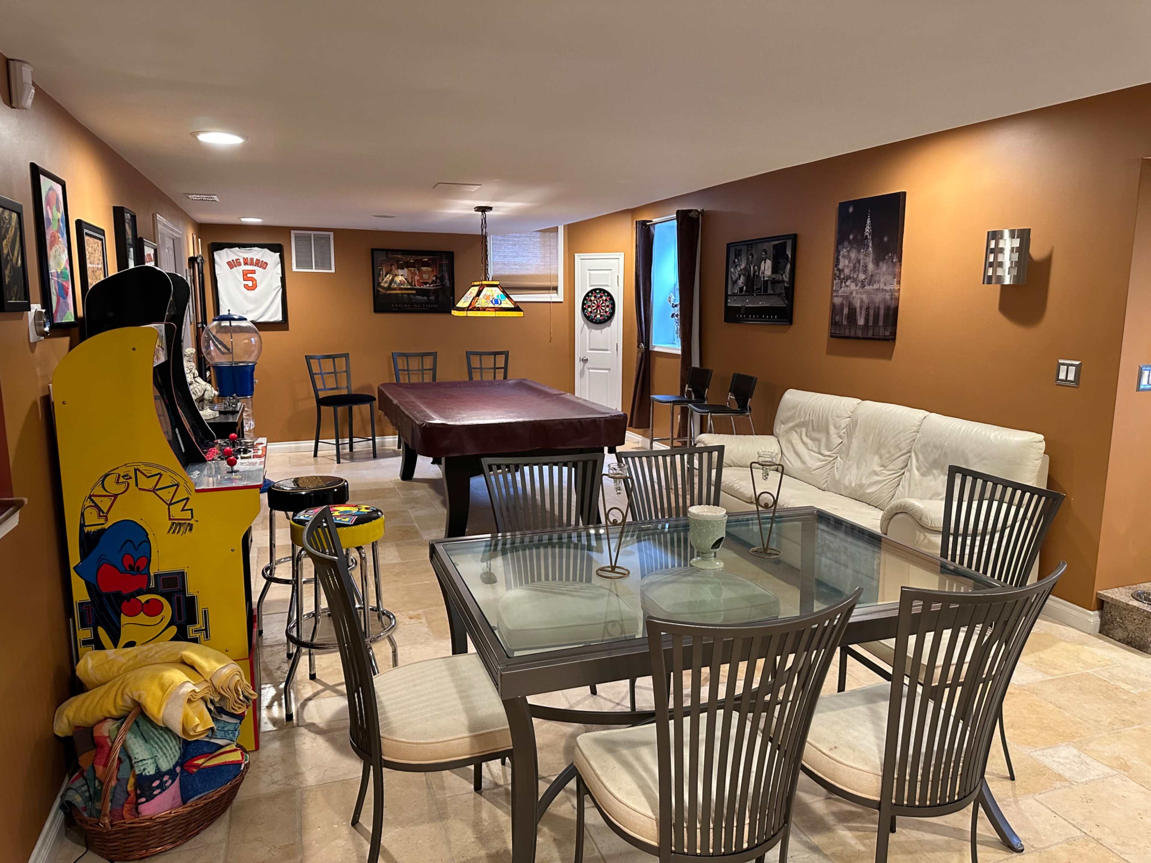 A basement recreational area featuring a dining table, a pool table, an arcade game machine, and various wall decorations.