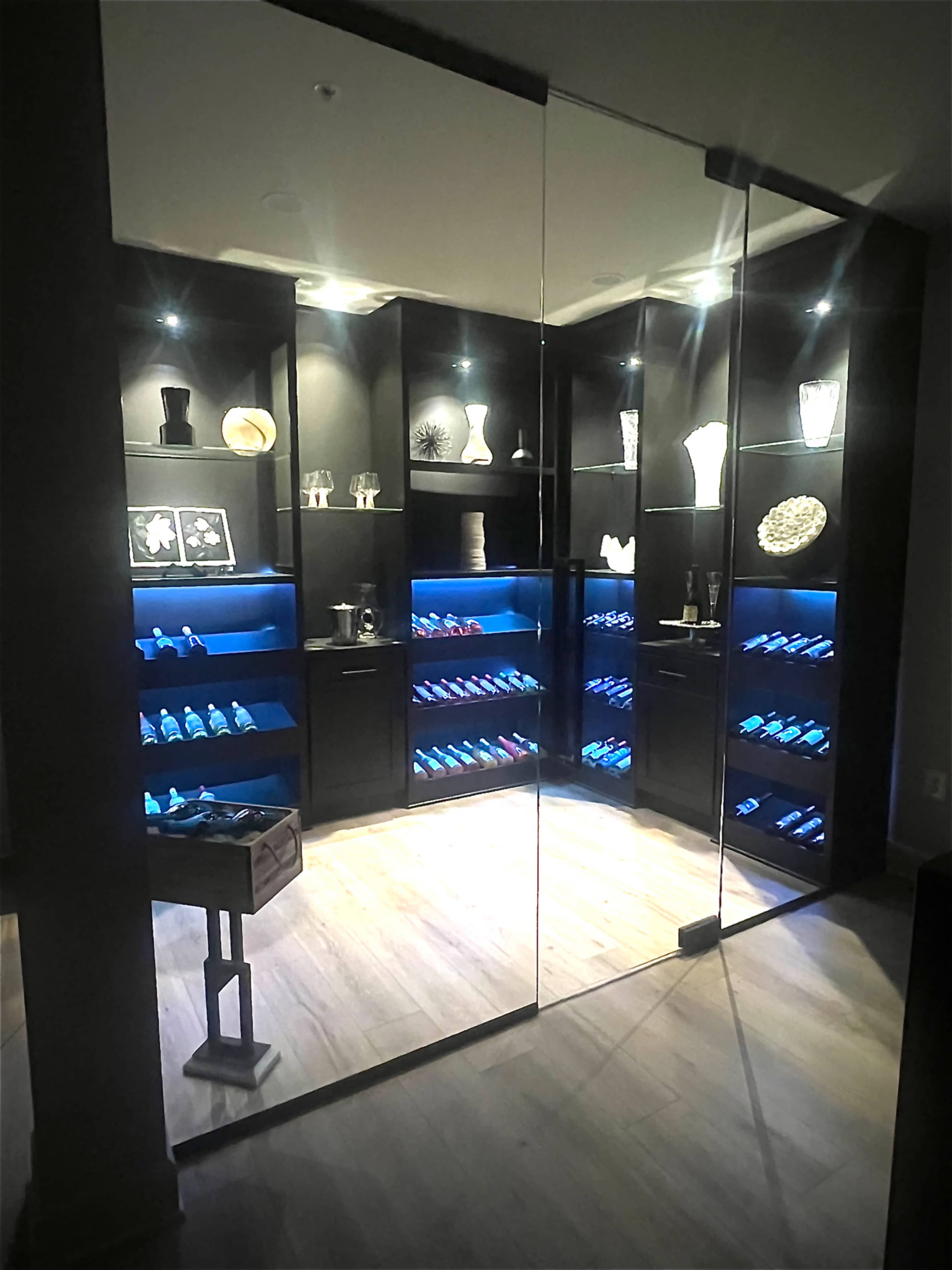 The image shows a modern display room with glass walls, featuring shelves filled with decorative items and illuminated by blue lights.