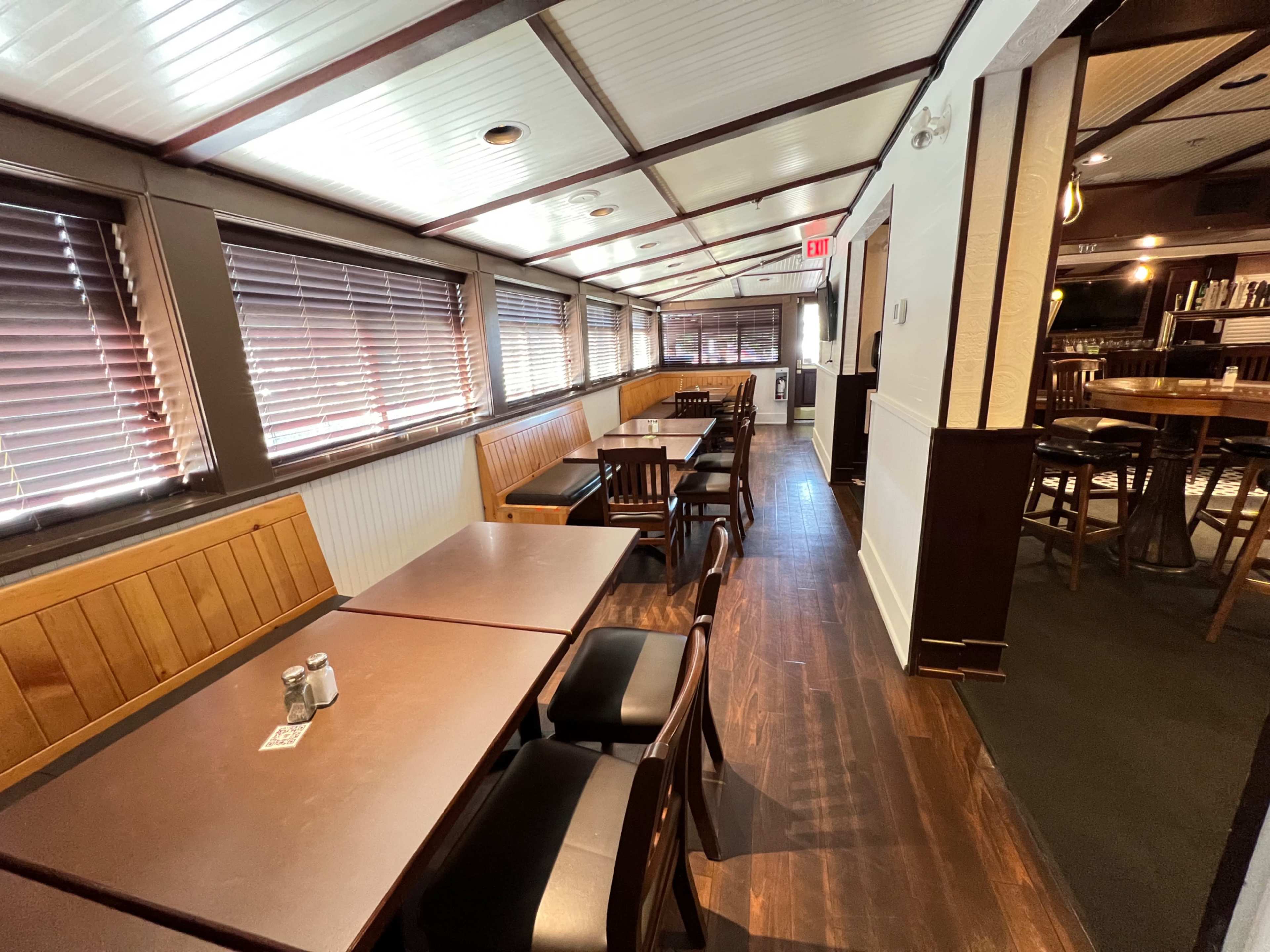 A narrow restaurant interior with wooden booths and tables along one side and an entrance visible at the end of the hallway.