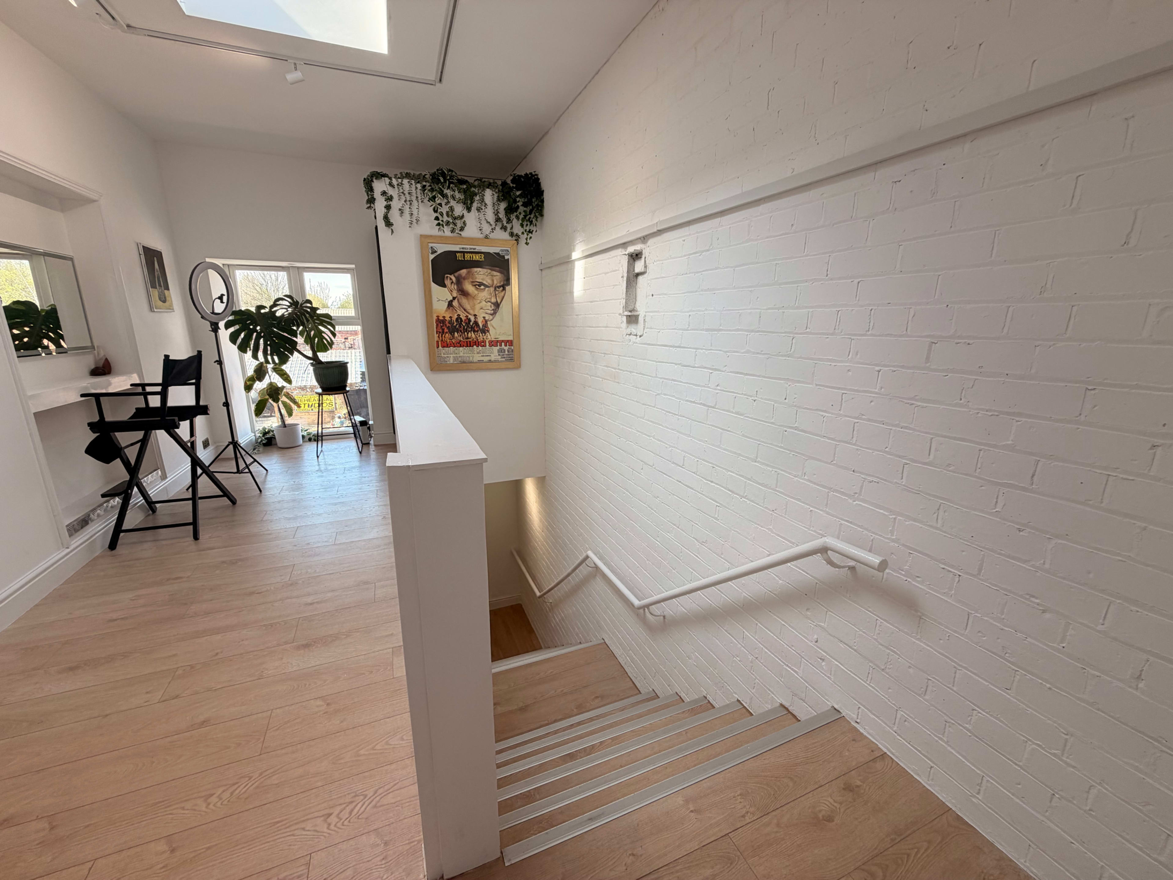 A bright, modern staircase leads down from a light-filled hallway adorned with plants and wall art.