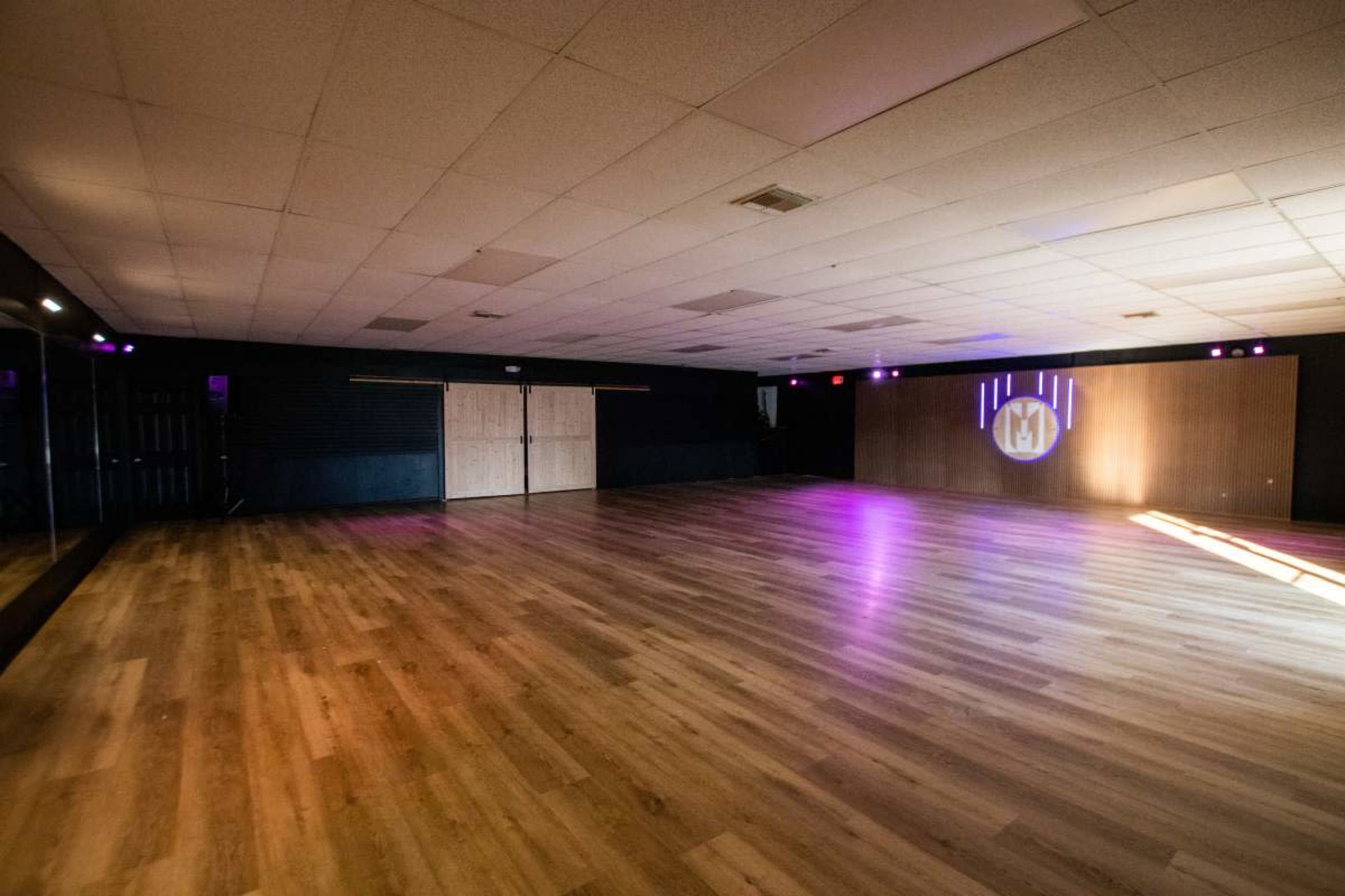 The image shows an empty dance studio with wooden flooring and a large wall projection.