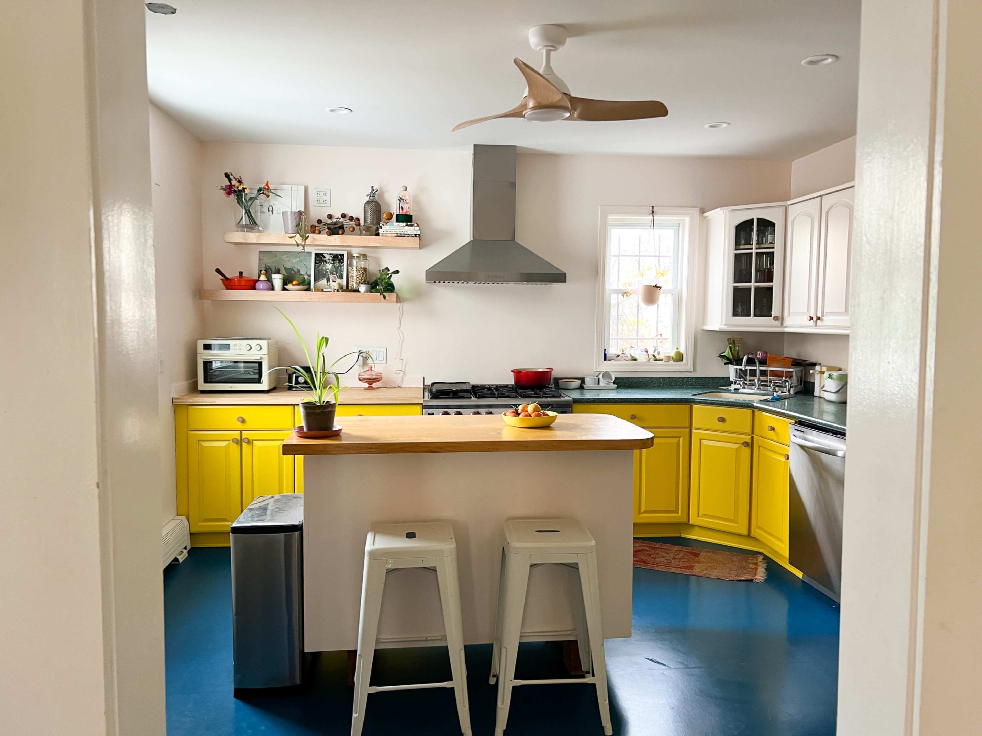 A bright kitchen features yellow cabinets, a central island with bar stools, and modern appliances.