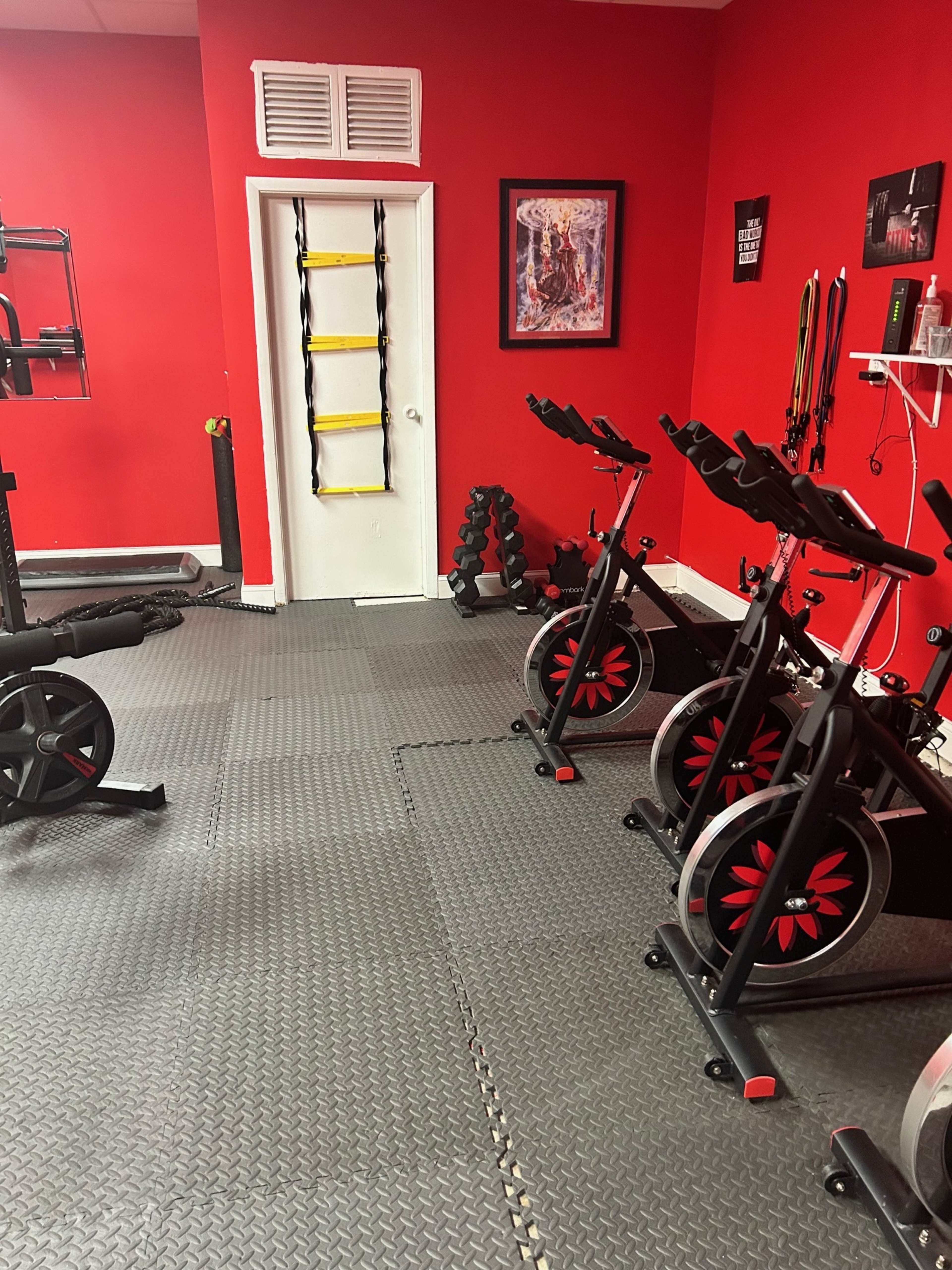 The image shows a gym area with black exercise equipment, including stationary bikes and weights, set against red walls and a patterned rubber floor.
