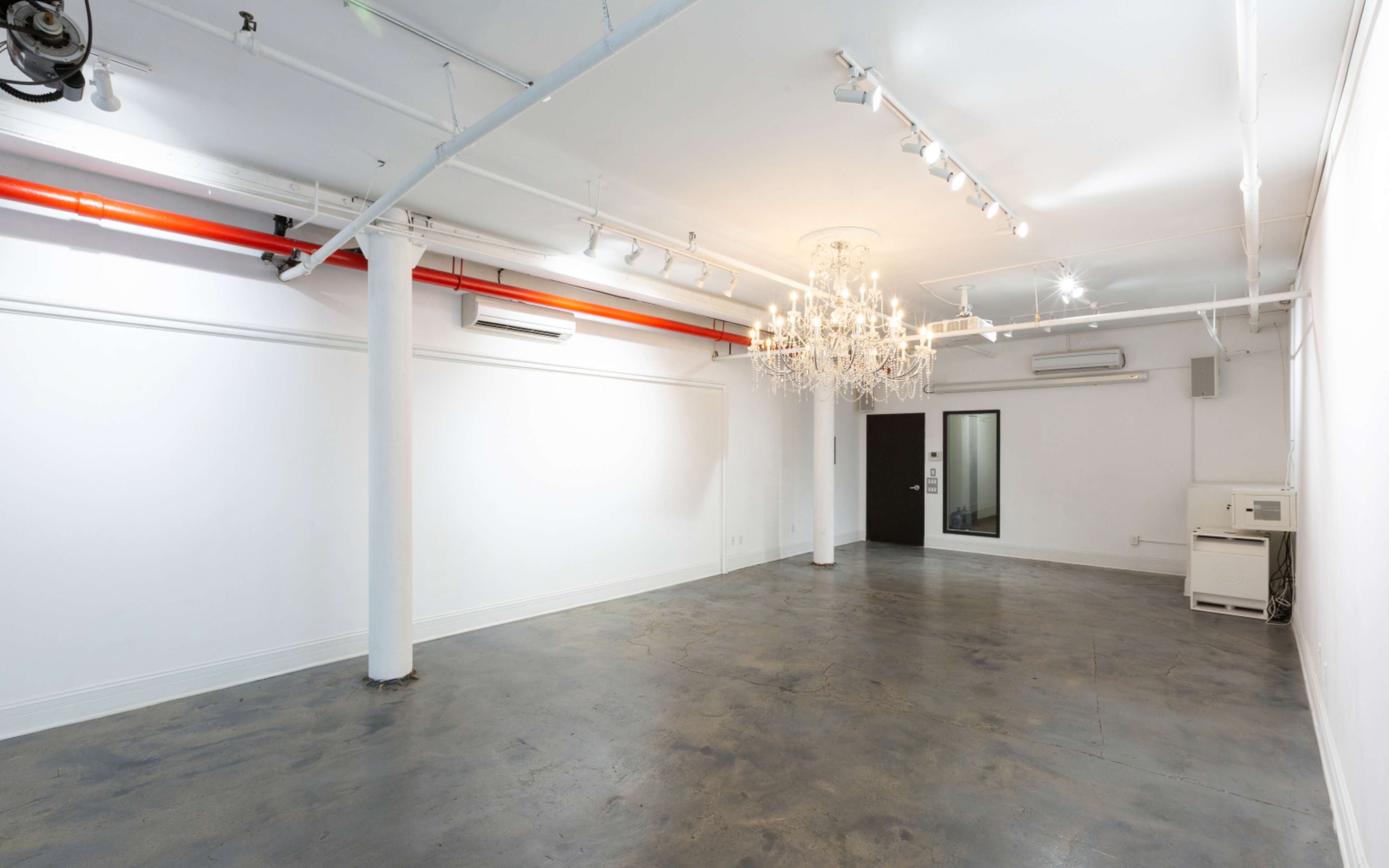 An empty room with polished concrete floors, white walls, and a large chandelier hanging from the ceiling.