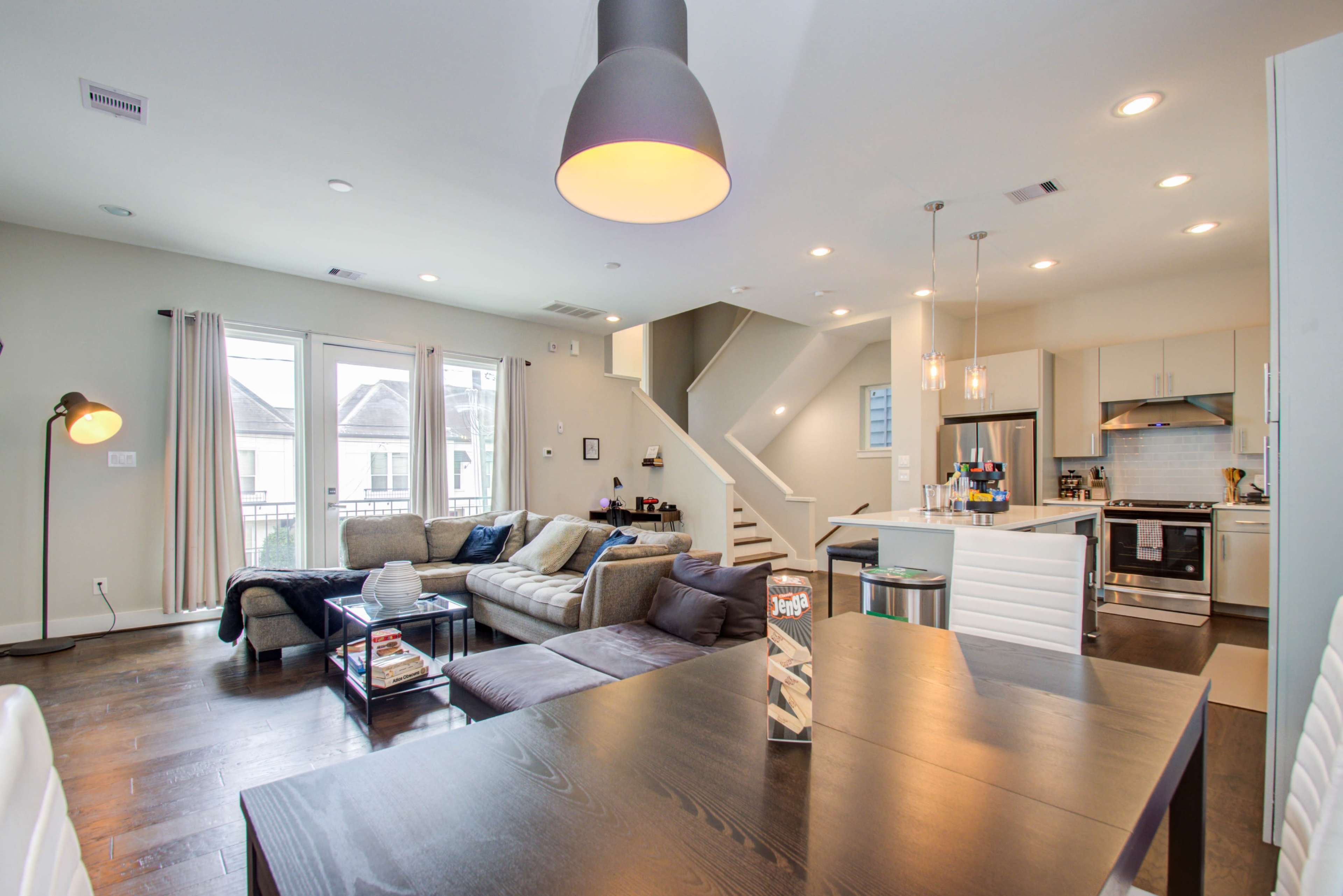A modern open-concept living space features a sectional sofa, a dining table, and a kitchen with stainless steel appliances.