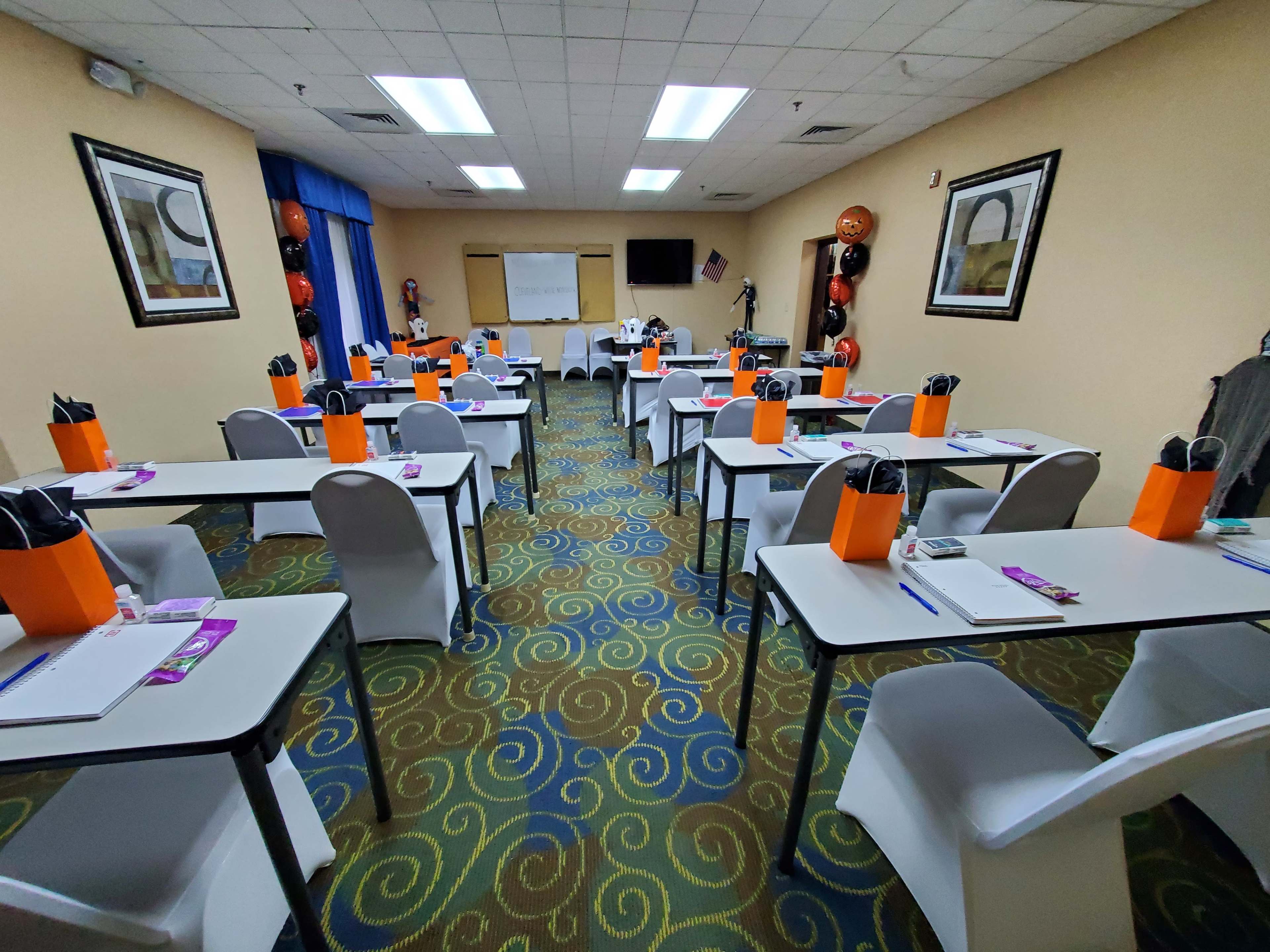 A conference room is set up with rows of tables and chairs, featuring orange gift bags on each table and decorations for an event.