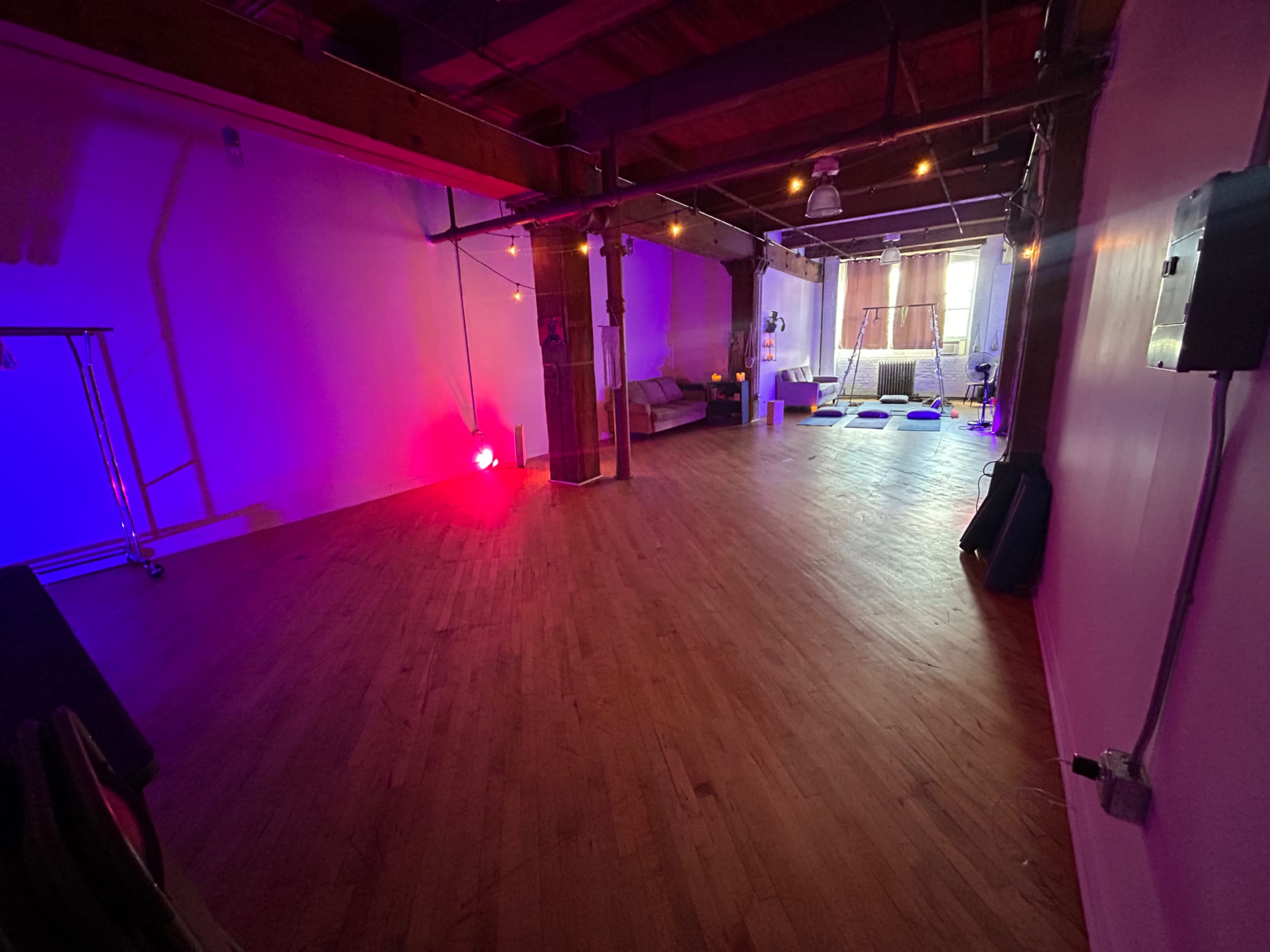 An empty studio space with wooden floors, colorful lighting, and several large windows.