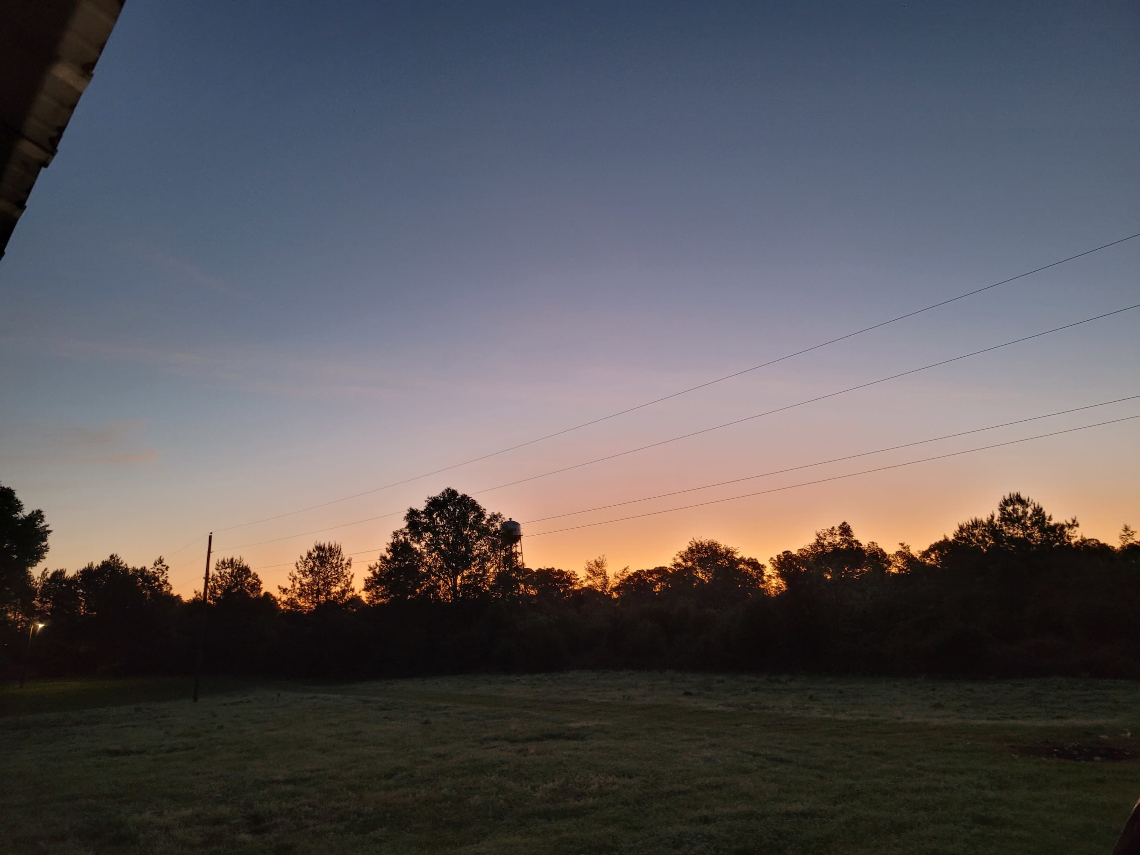 The image shows a landscape at dusk with silhouetted trees and utility poles against a gradient sky transitioning from orange to blue.