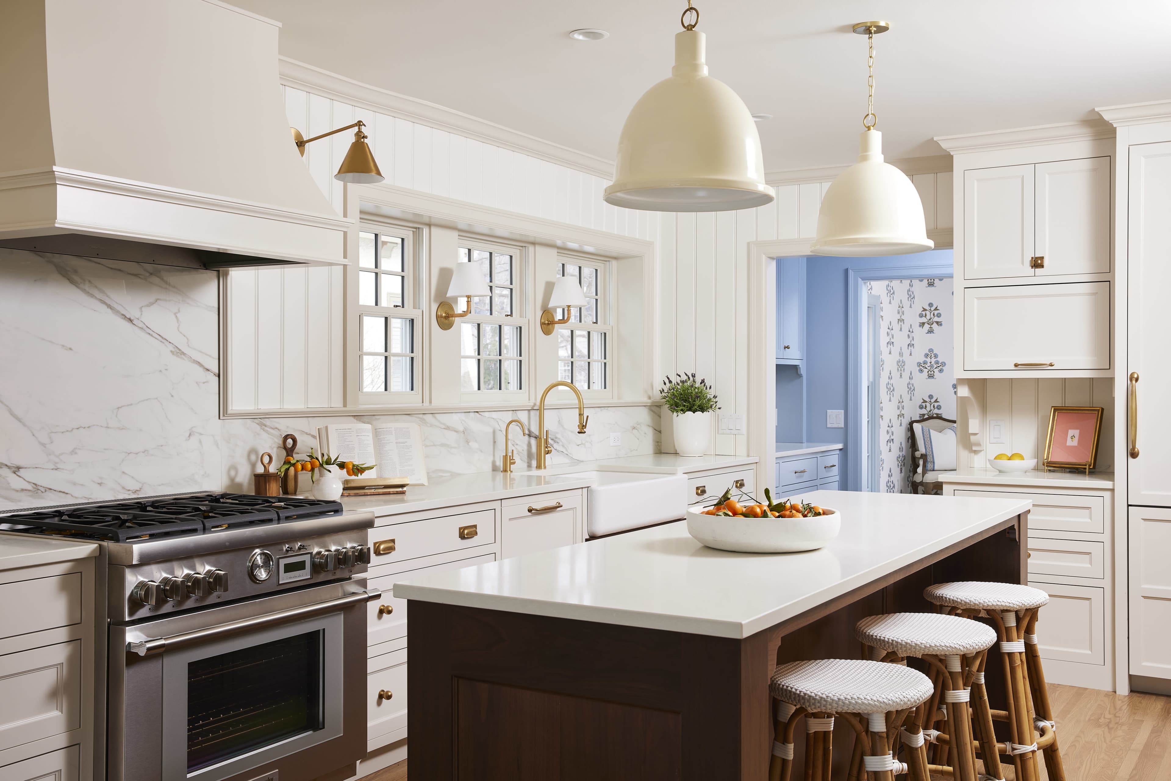 The kitchen features a large island with three stools, stone countertops, white cabinets, and modern brass fixtures.