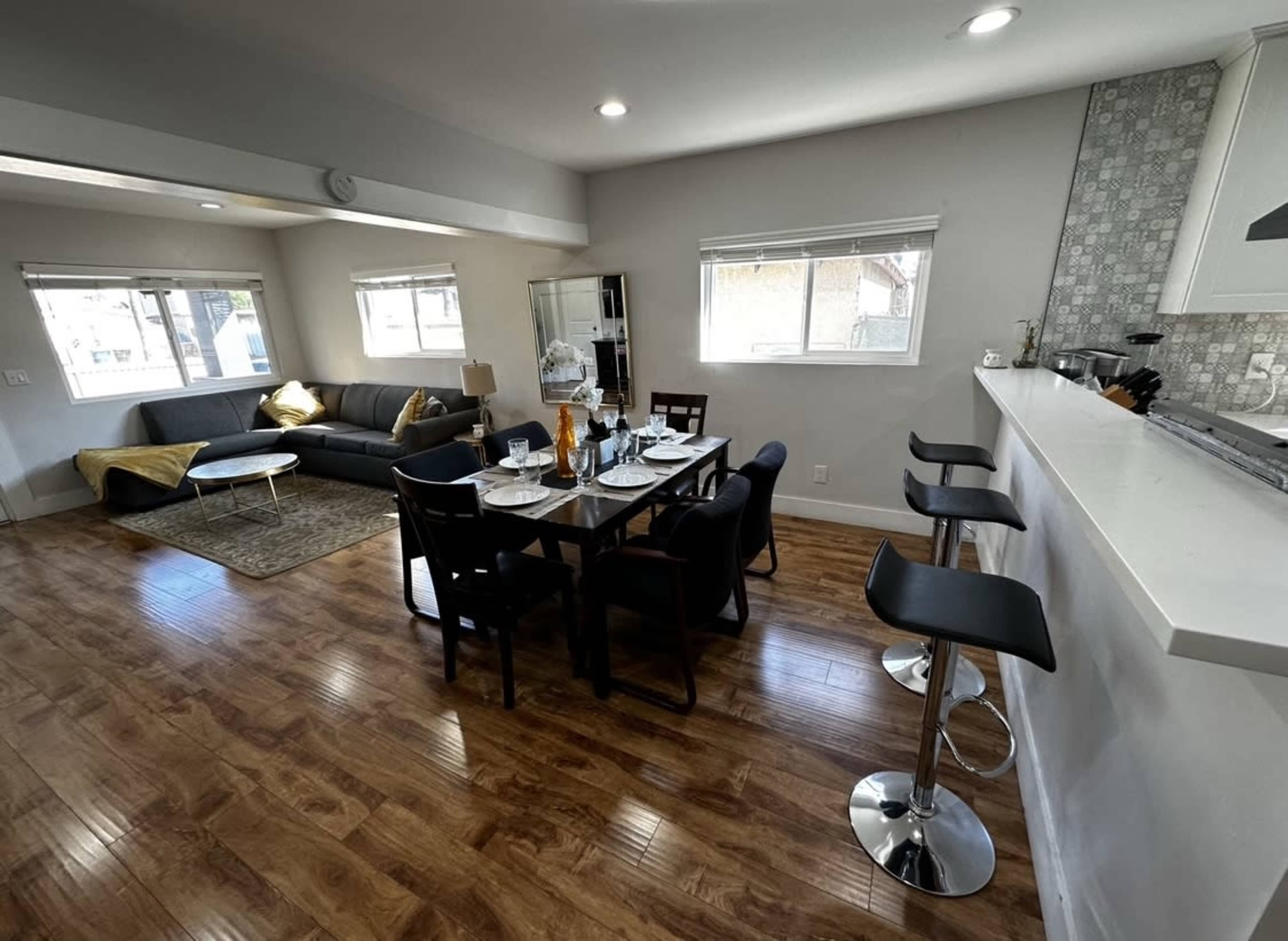 A modern living space with a dining area featuring a set table, a sofa, and bar seating adjacent to a kitchen counter.