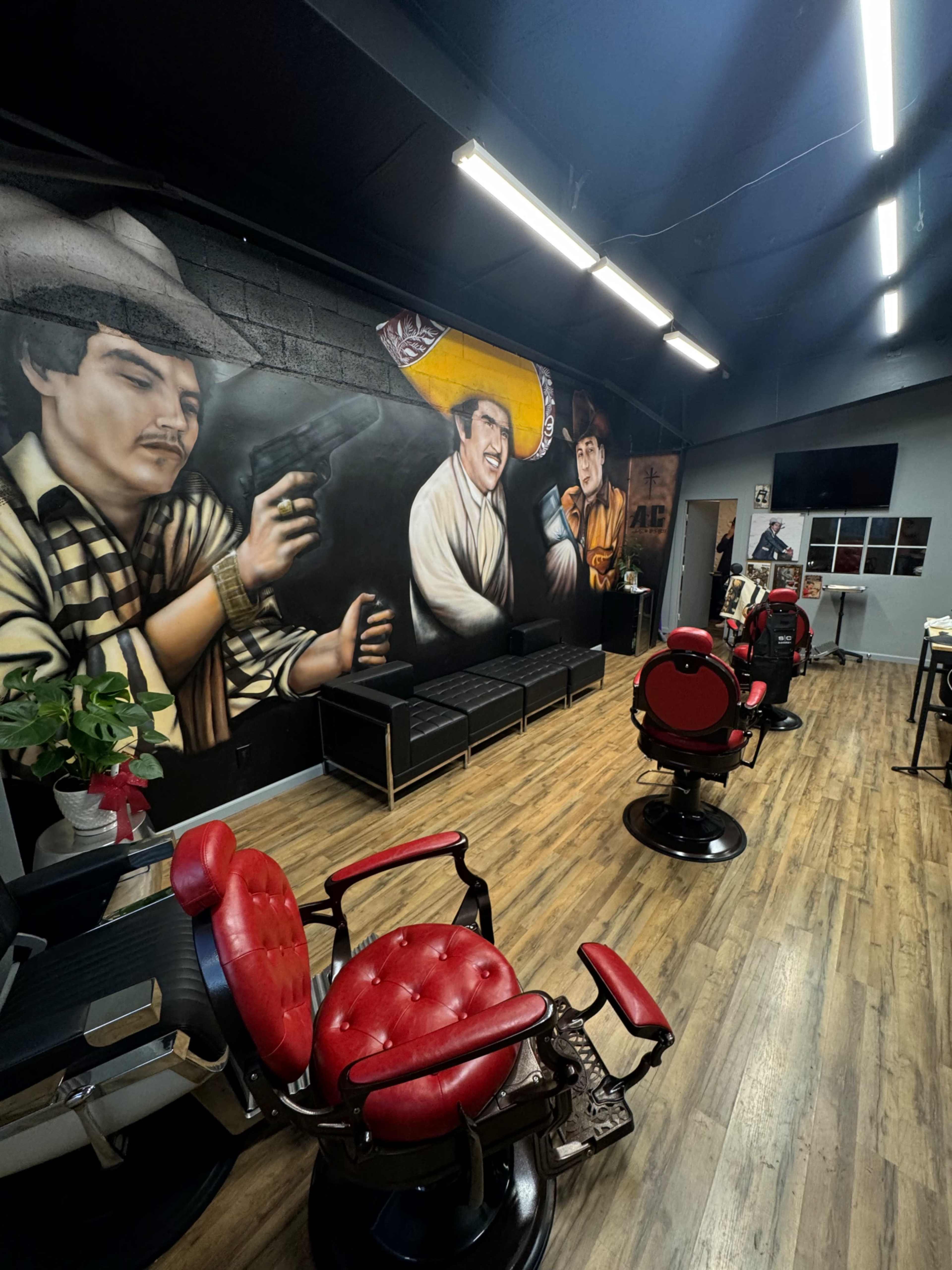 The interior of a barbershop features vintage-style barber chairs, a mural on the wall depicting two men, and a modern reception area.