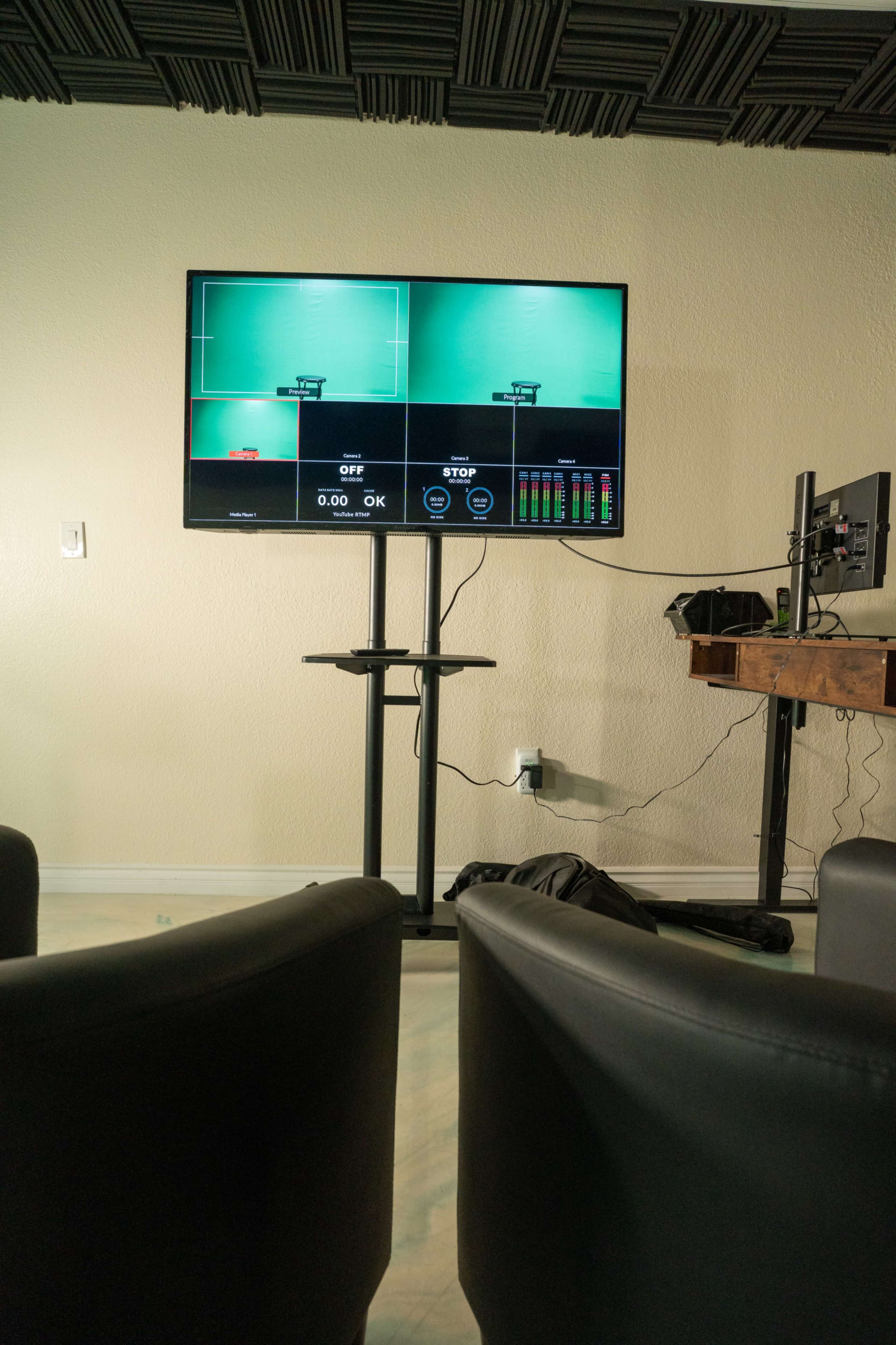 A large display mounted on a wall shows a green screen interface with controls labeled "OFF" and "STOP," while two black chairs face the screen.