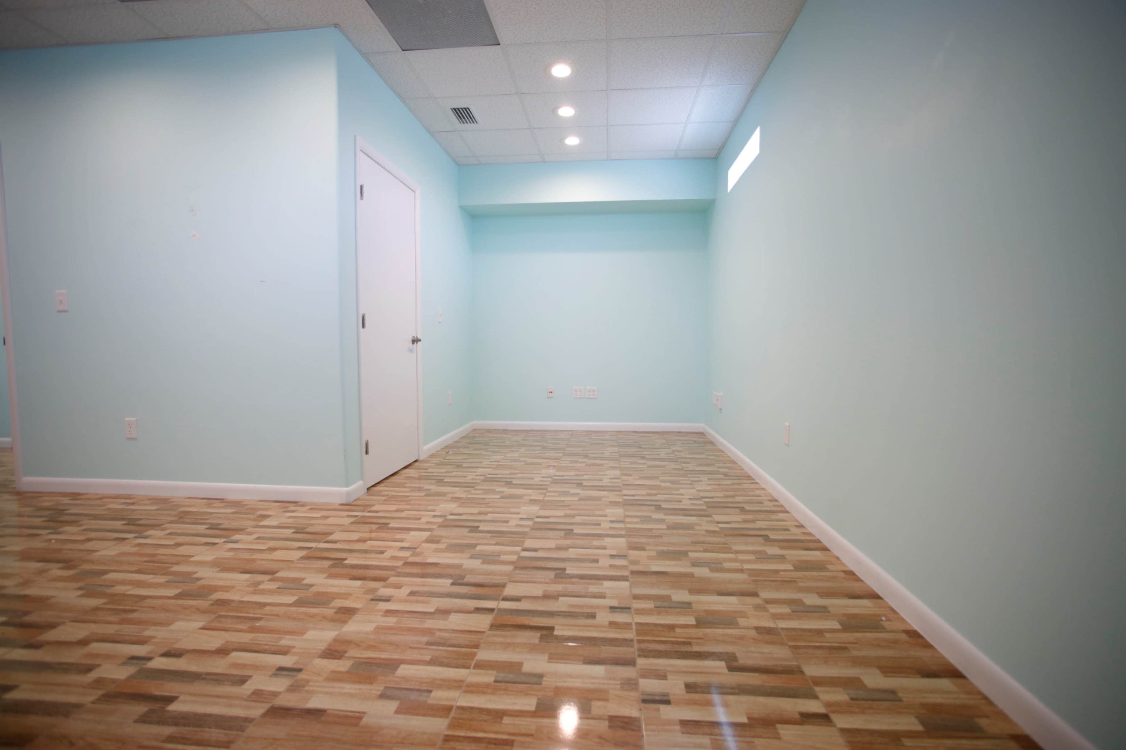 The image shows a vacant room with light blue walls and a wooden floor.
