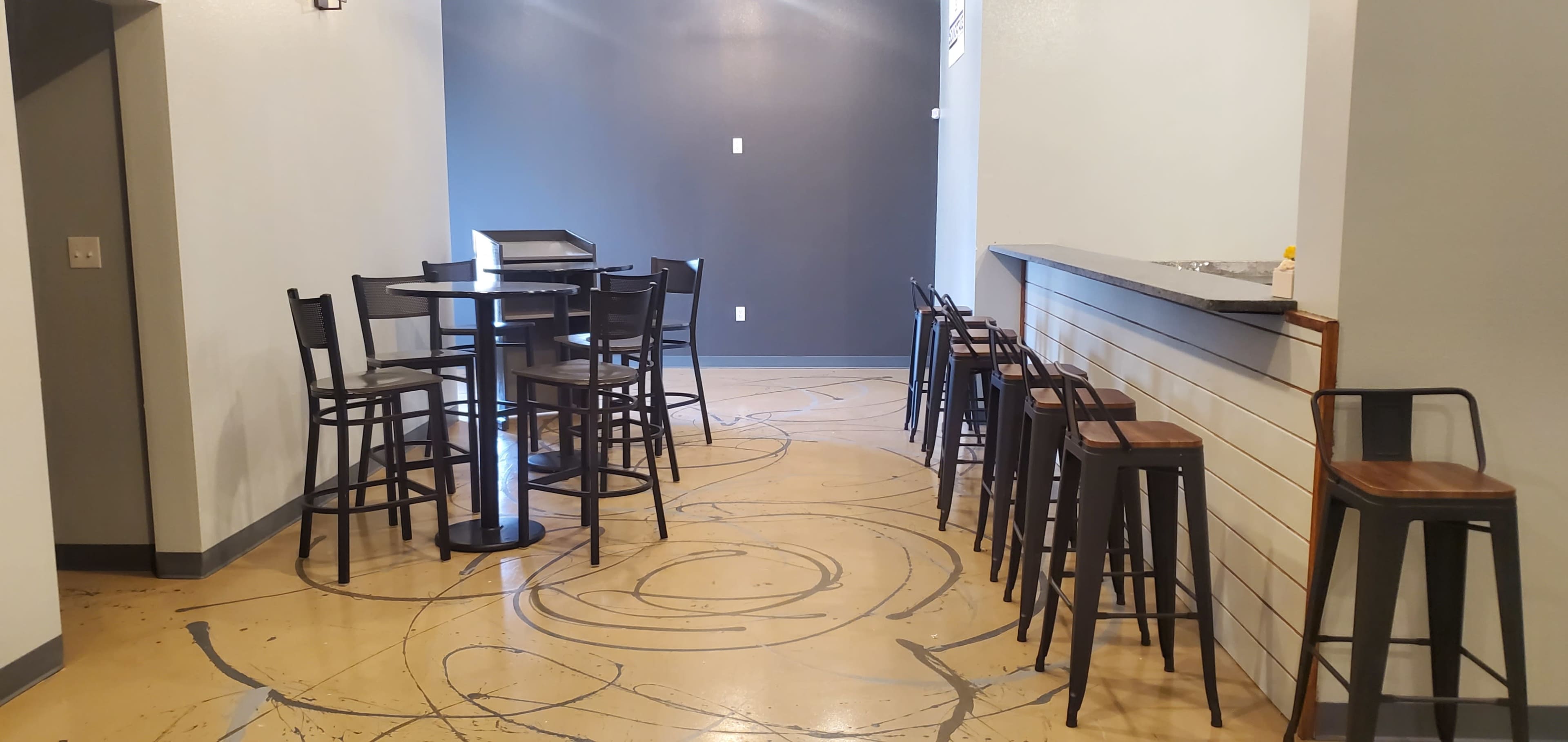 A modern, minimalist indoor space with a high table and stools on one side and a counter with bar stools along the wall.