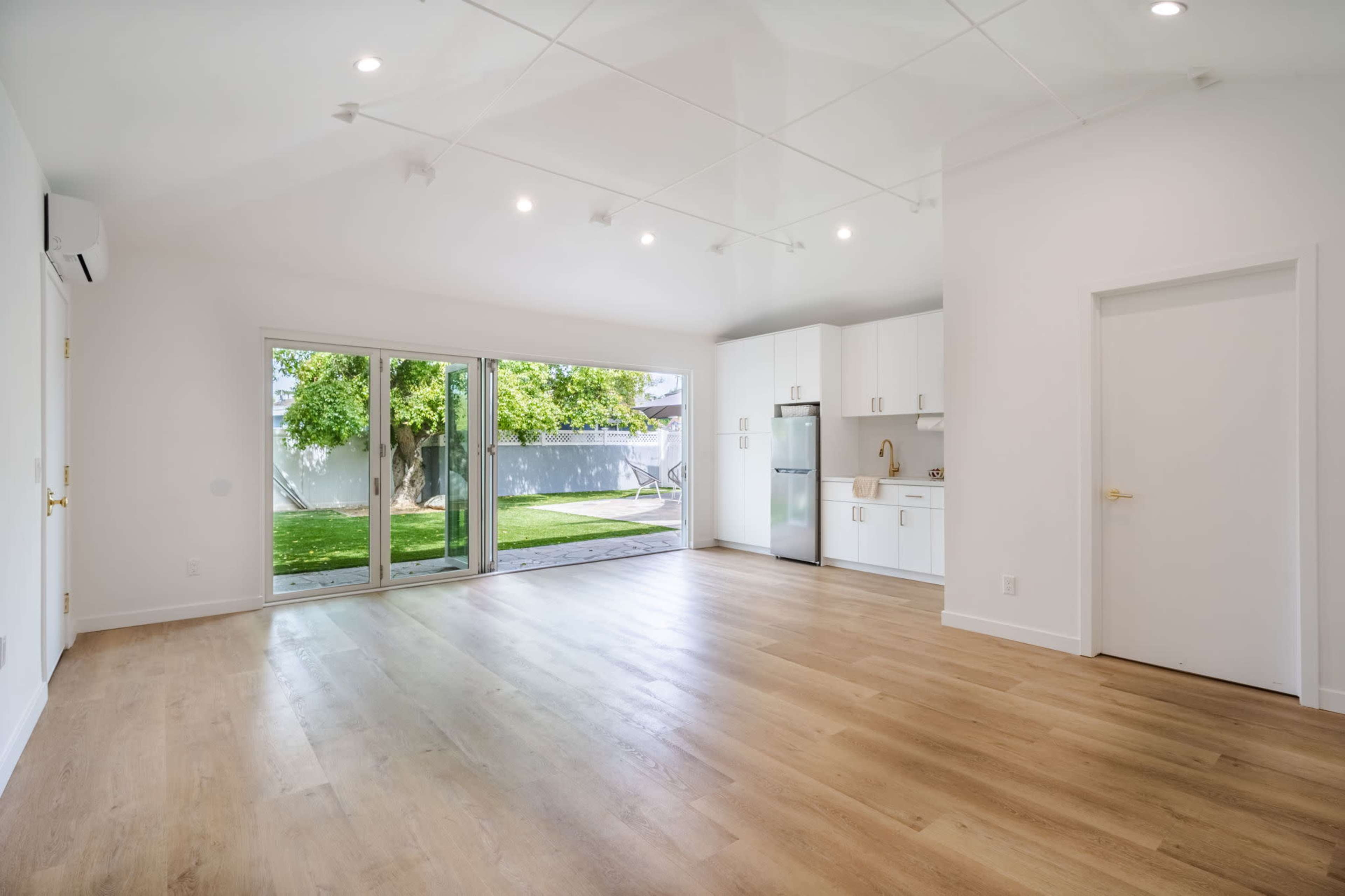 A bright, empty living space with wood flooring and large sliding glass doors leading to a green yard.