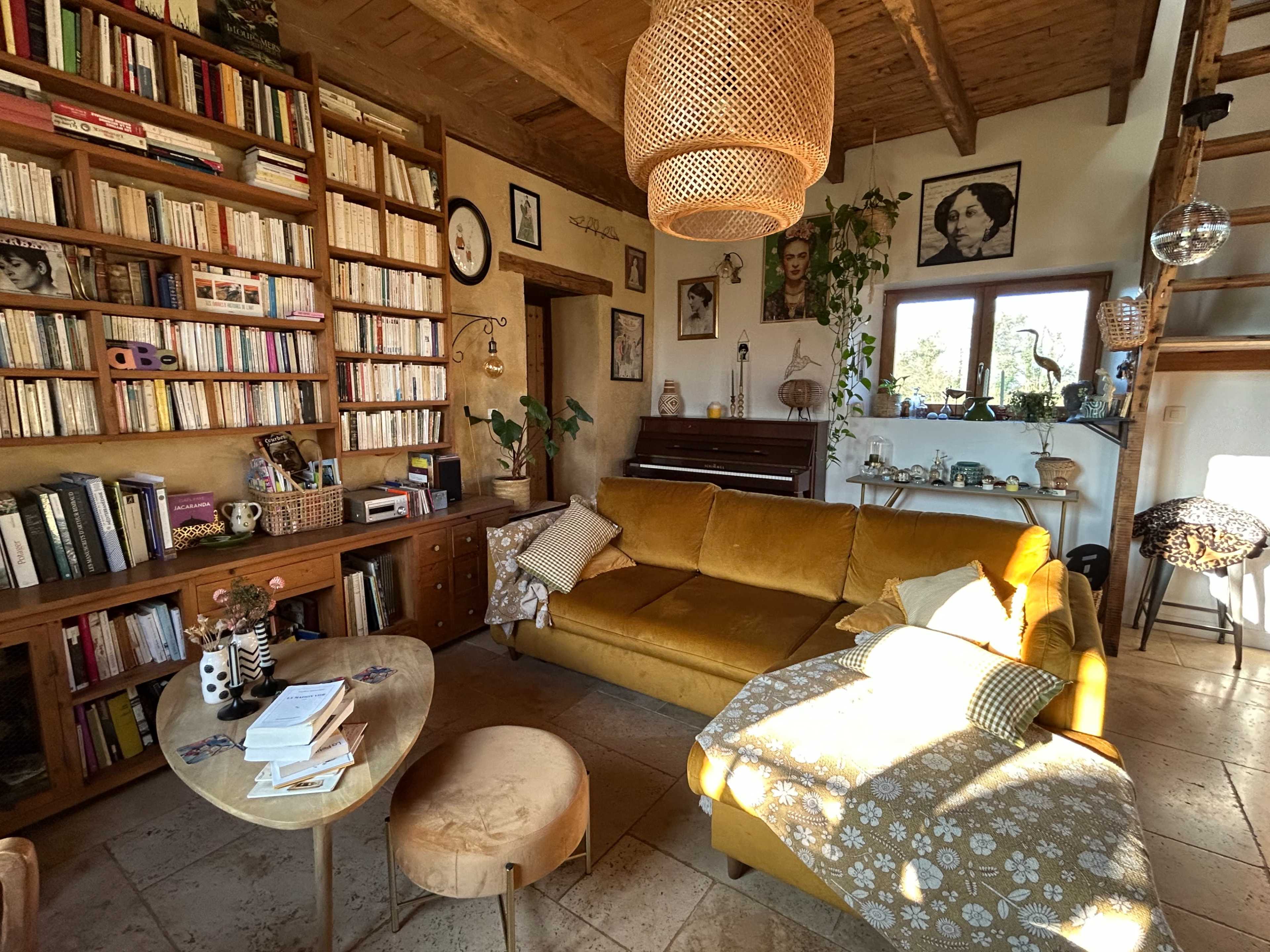 The image shows a cozy living room featuring a yellow sofa, a wooden bookshelf filled with books, and various decorations including plants and framed photographs.