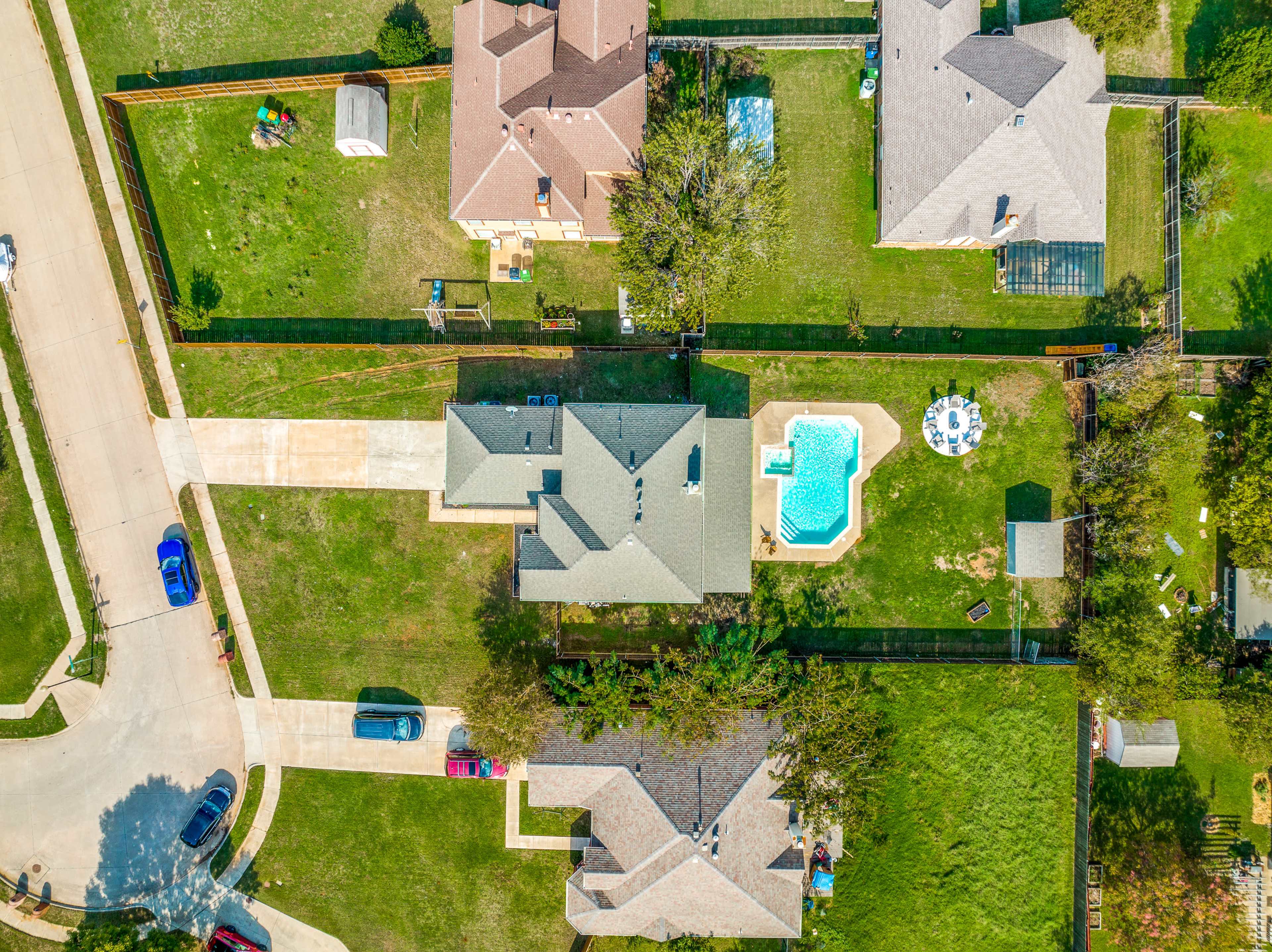 Aerial view of several houses on a suburban street, with a backyard pool visible in one of the yards.