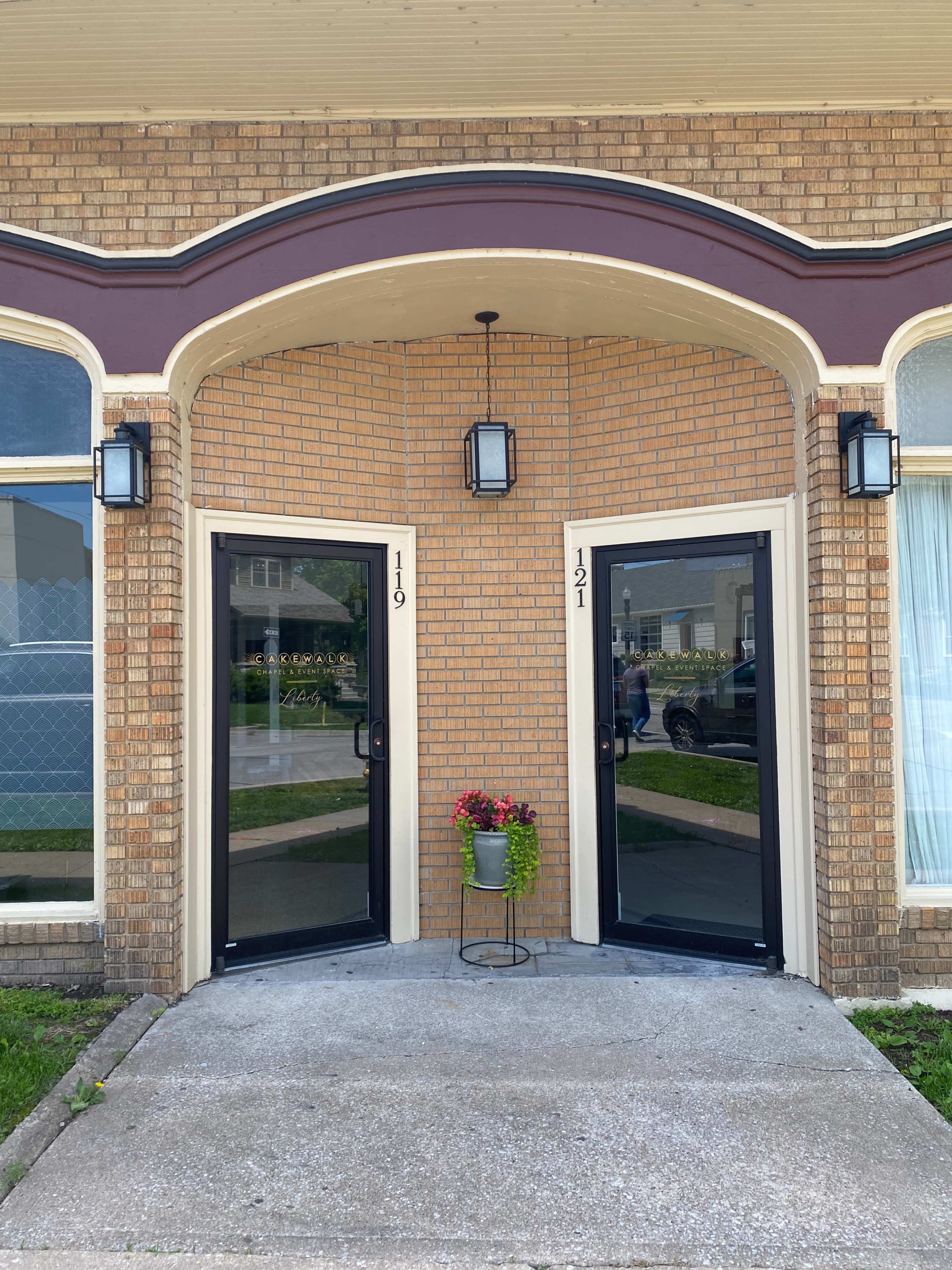 The image shows a brick building entrance with two black doors labeled "119" and "121," each accompanied by a potted plant.