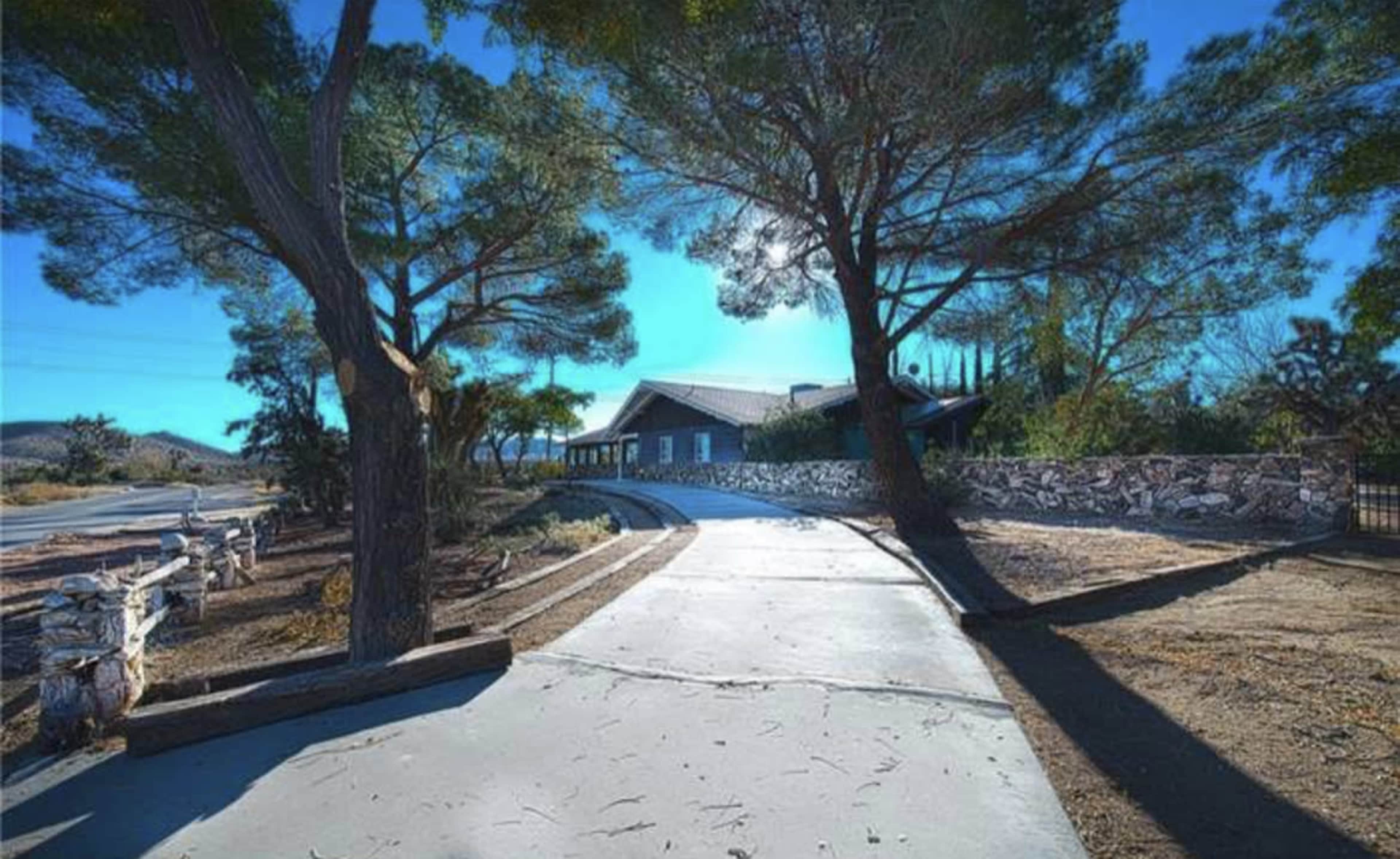A winding concrete driveway leads to a house surrounded by trees against a blue sky.
