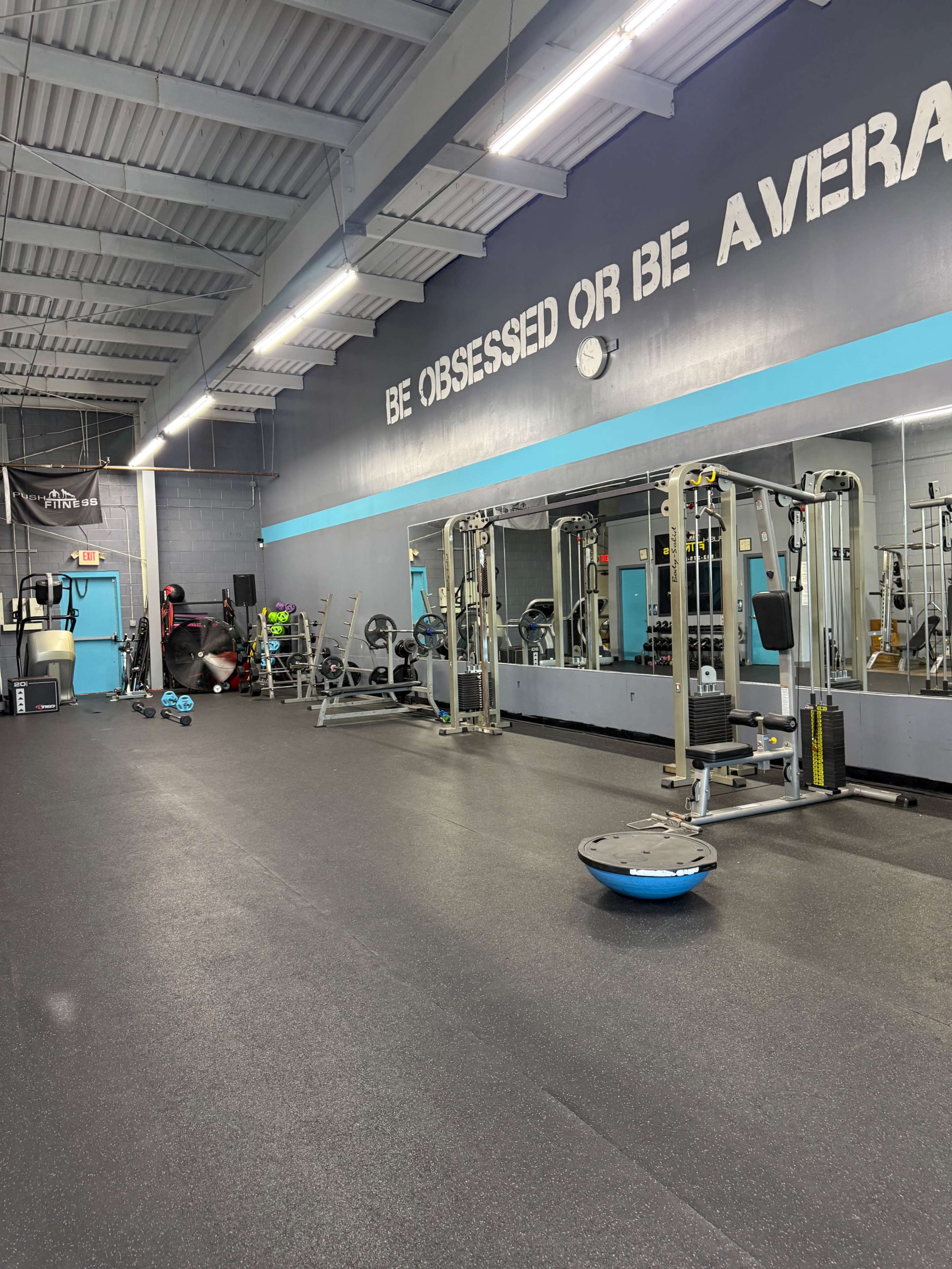 The image shows a gym interior featuring workout equipment, large mirrors, and motivational text on the wall.