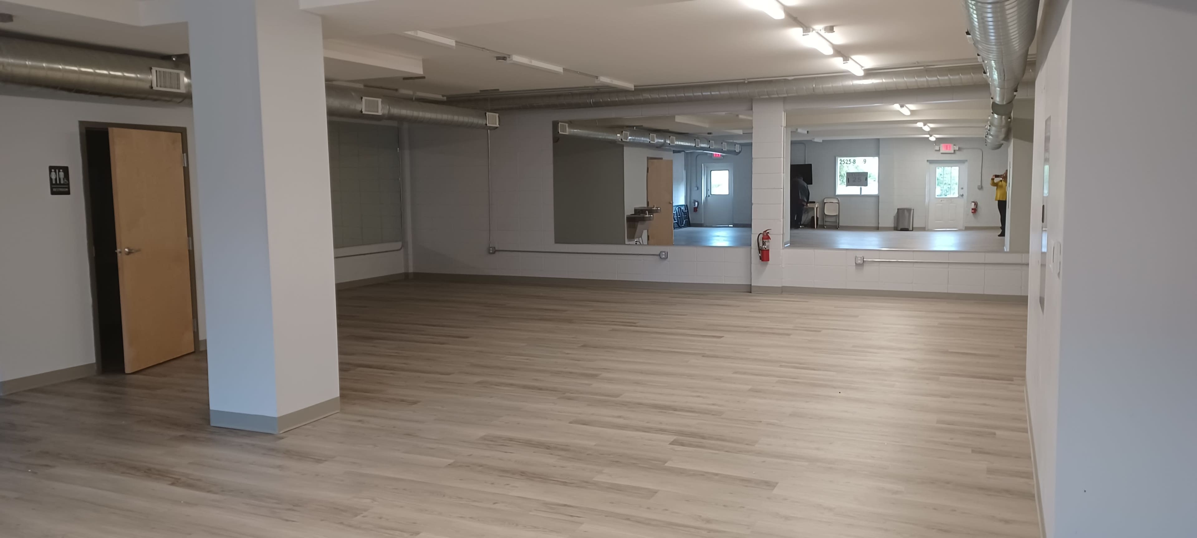 A spacious, empty room with light wooden flooring and large mirrors on one wall.
