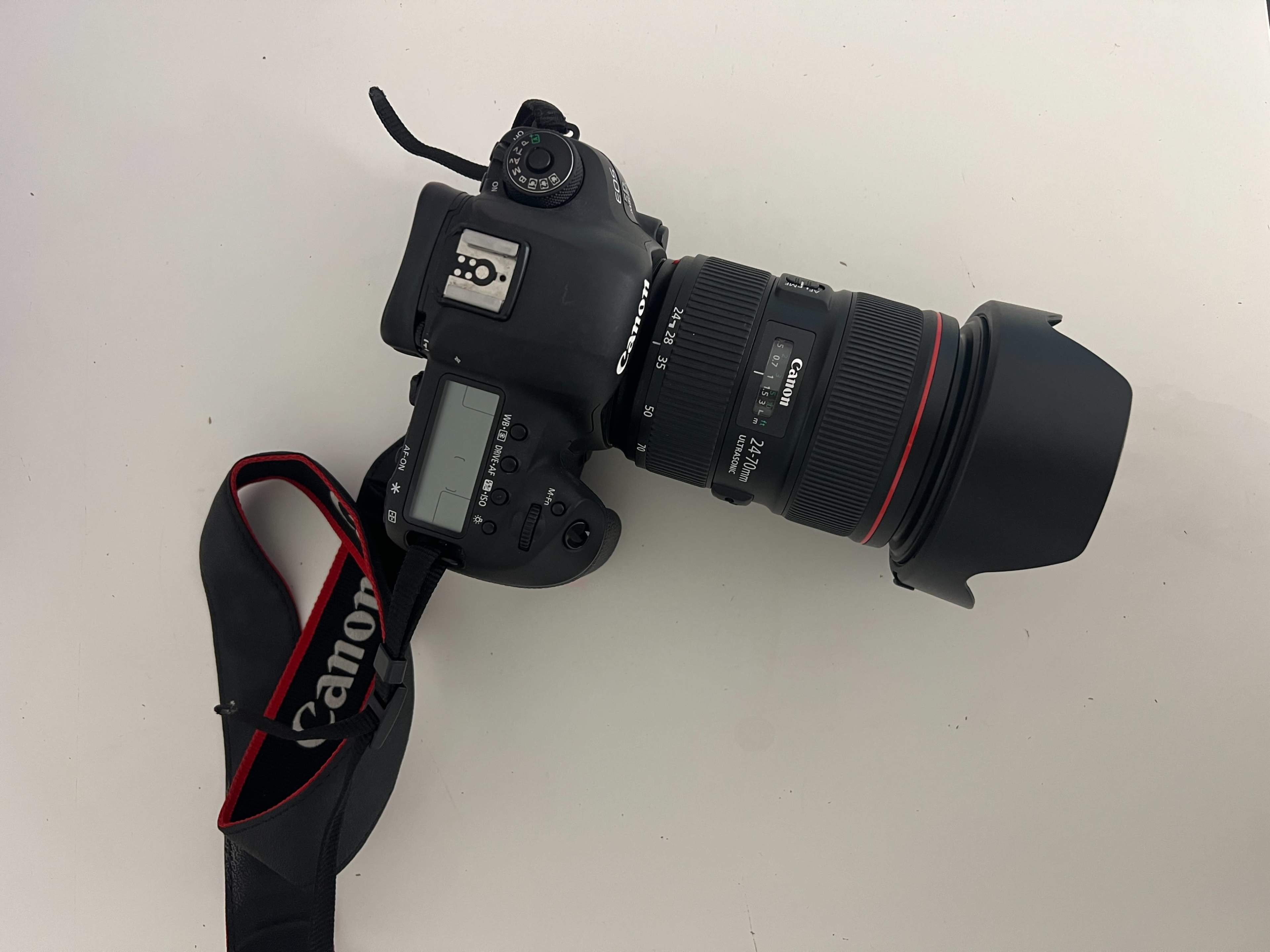 A Canon DSLR camera with a large lens is positioned on a white surface.