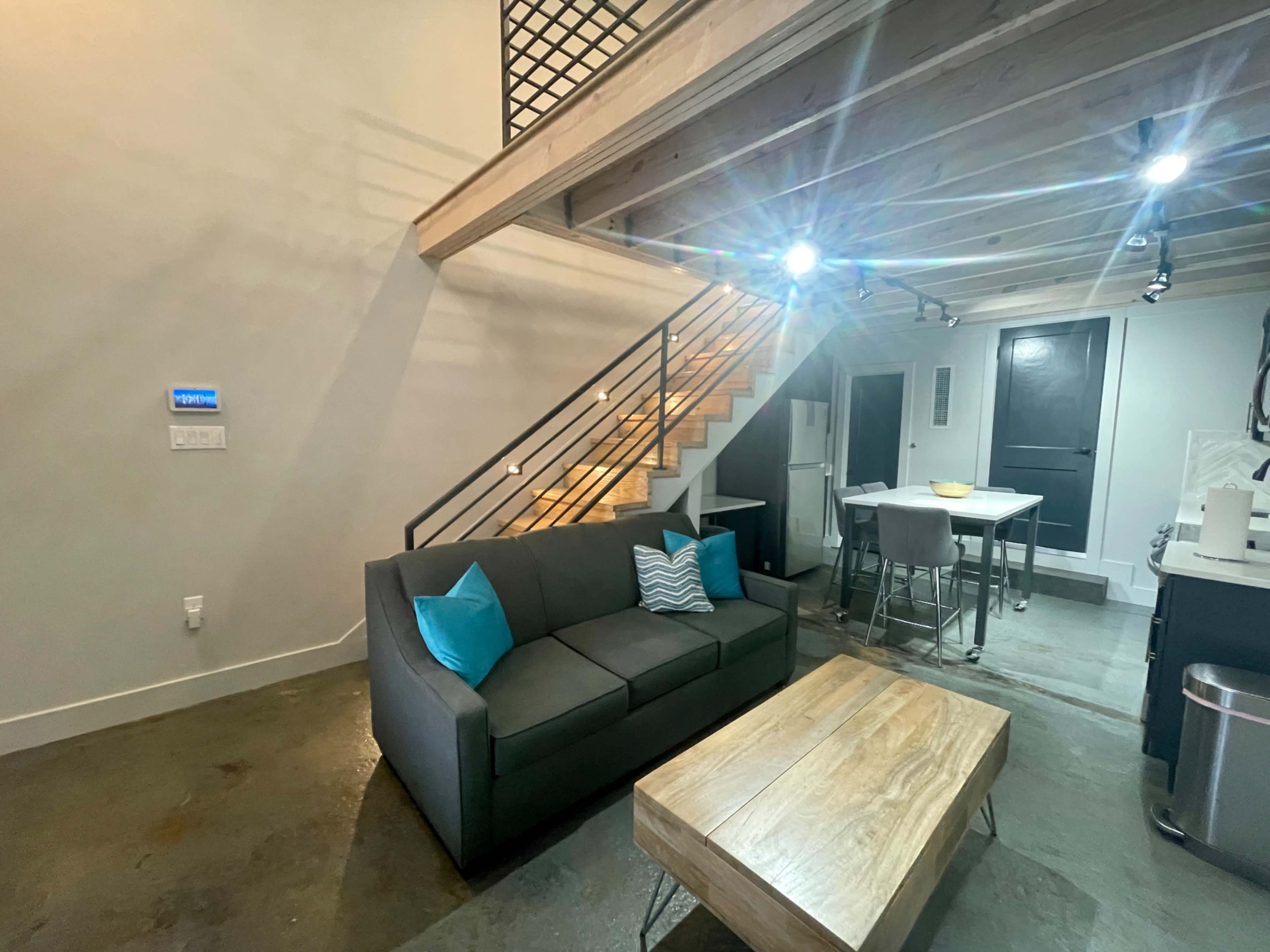 A modern living space featuring a gray sofa with teal cushions, a wooden coffee table, and a staircase leading to an upper level.