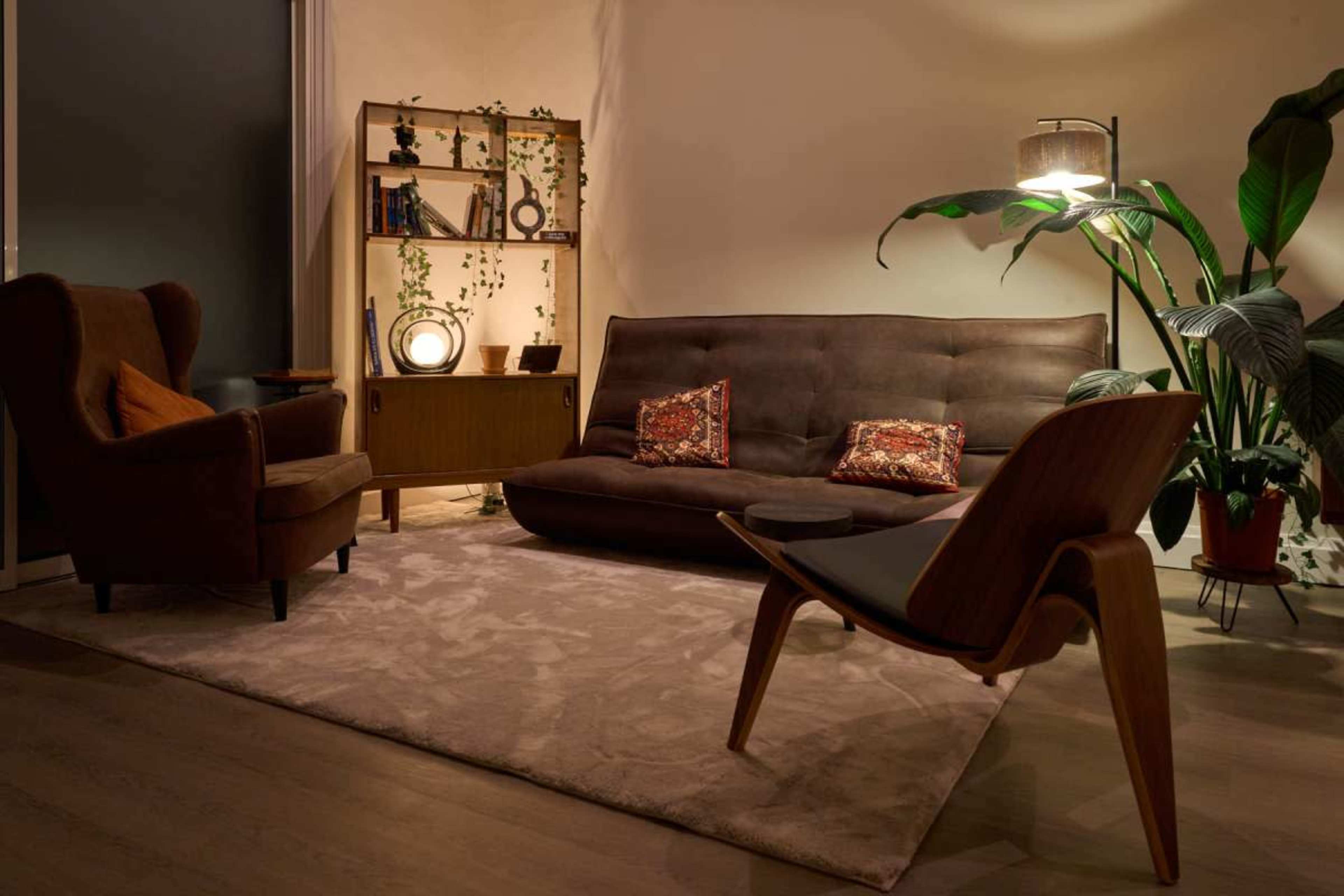 The image shows a cozy living room with a sofa, an armchair, a side table, and various decorative elements, illuminated by warm lighting.
