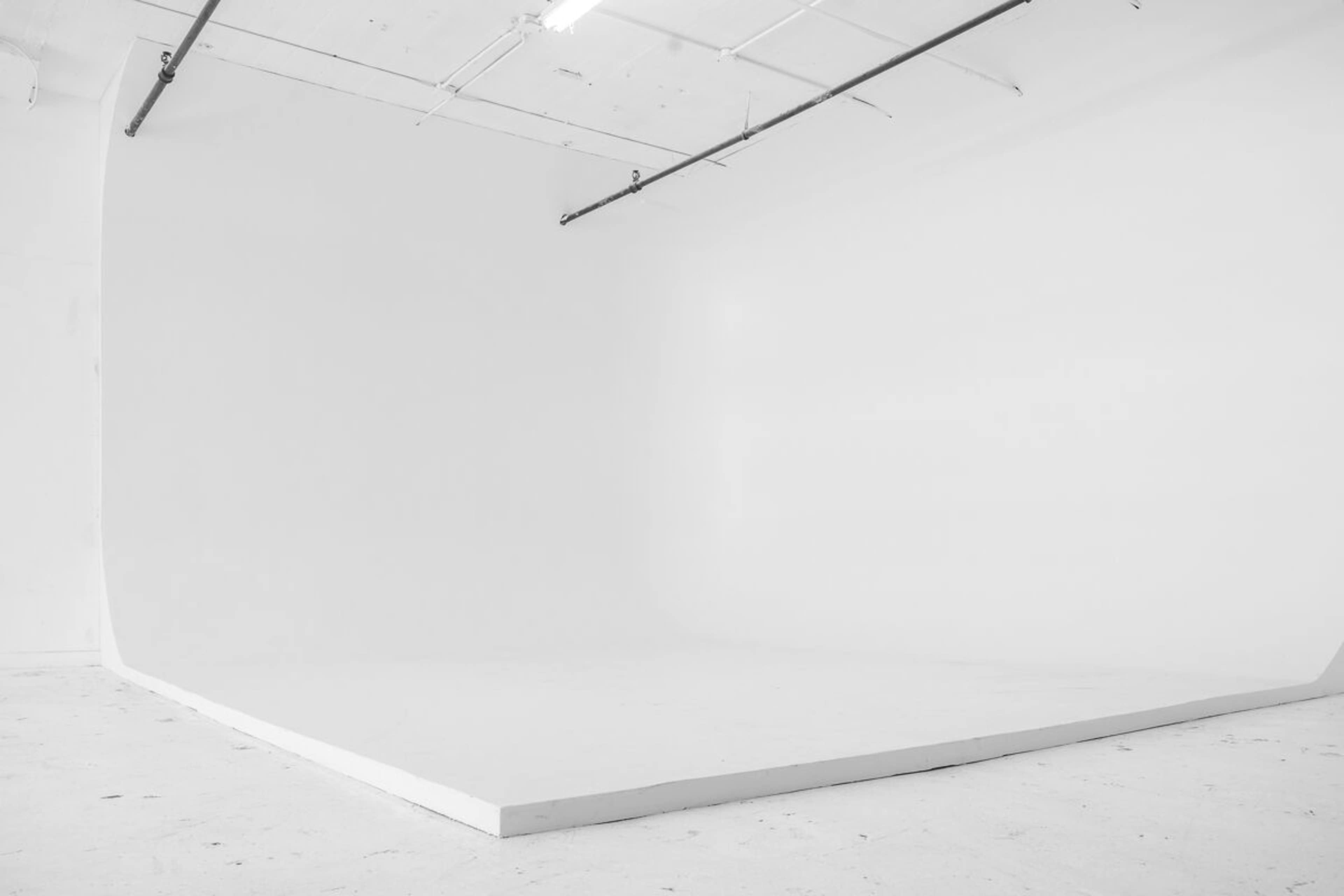 A spacious, minimalist white studio with a curved backdrop and a light-colored floor.