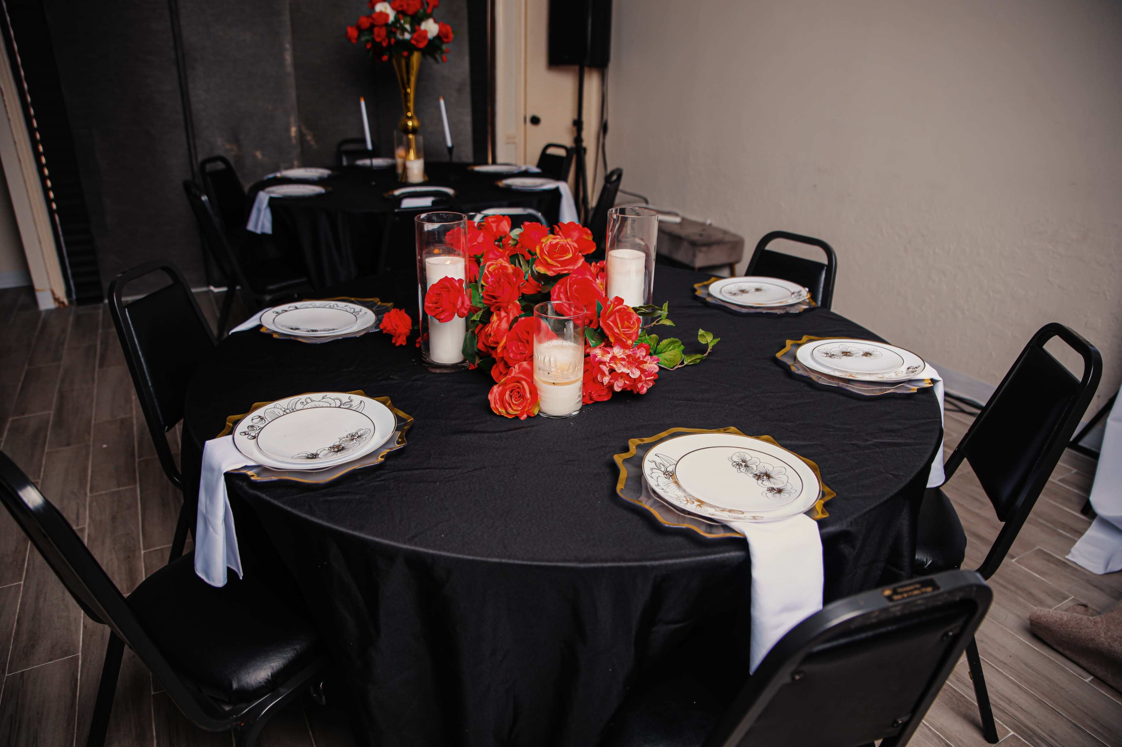 A black tablecloth covers a round table, set with decorative plates and a centerpiece of roses and candles.