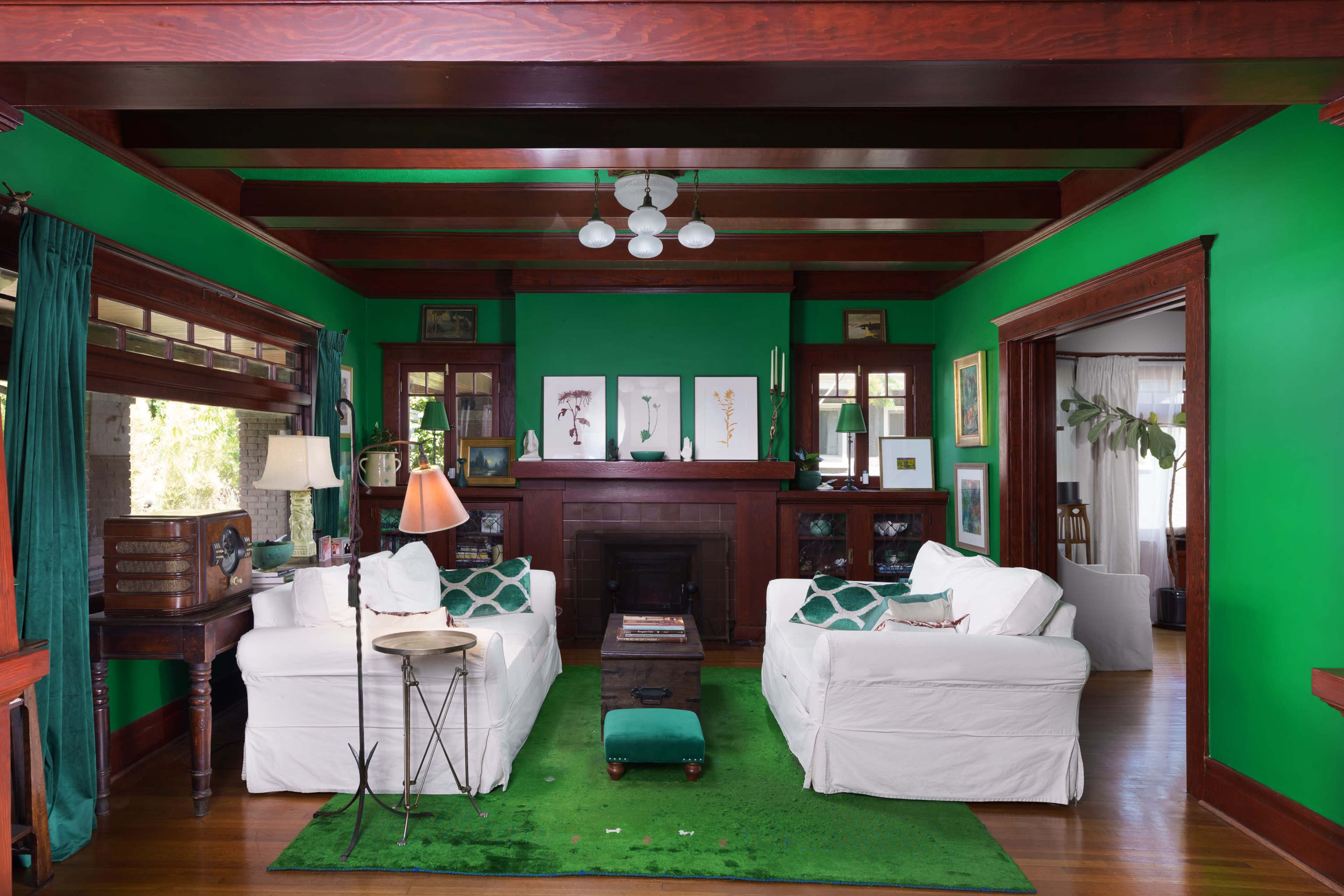 The living room features two white sofas, a green area rug, and bold green walls, complemented by wooden beams and framed artwork.
