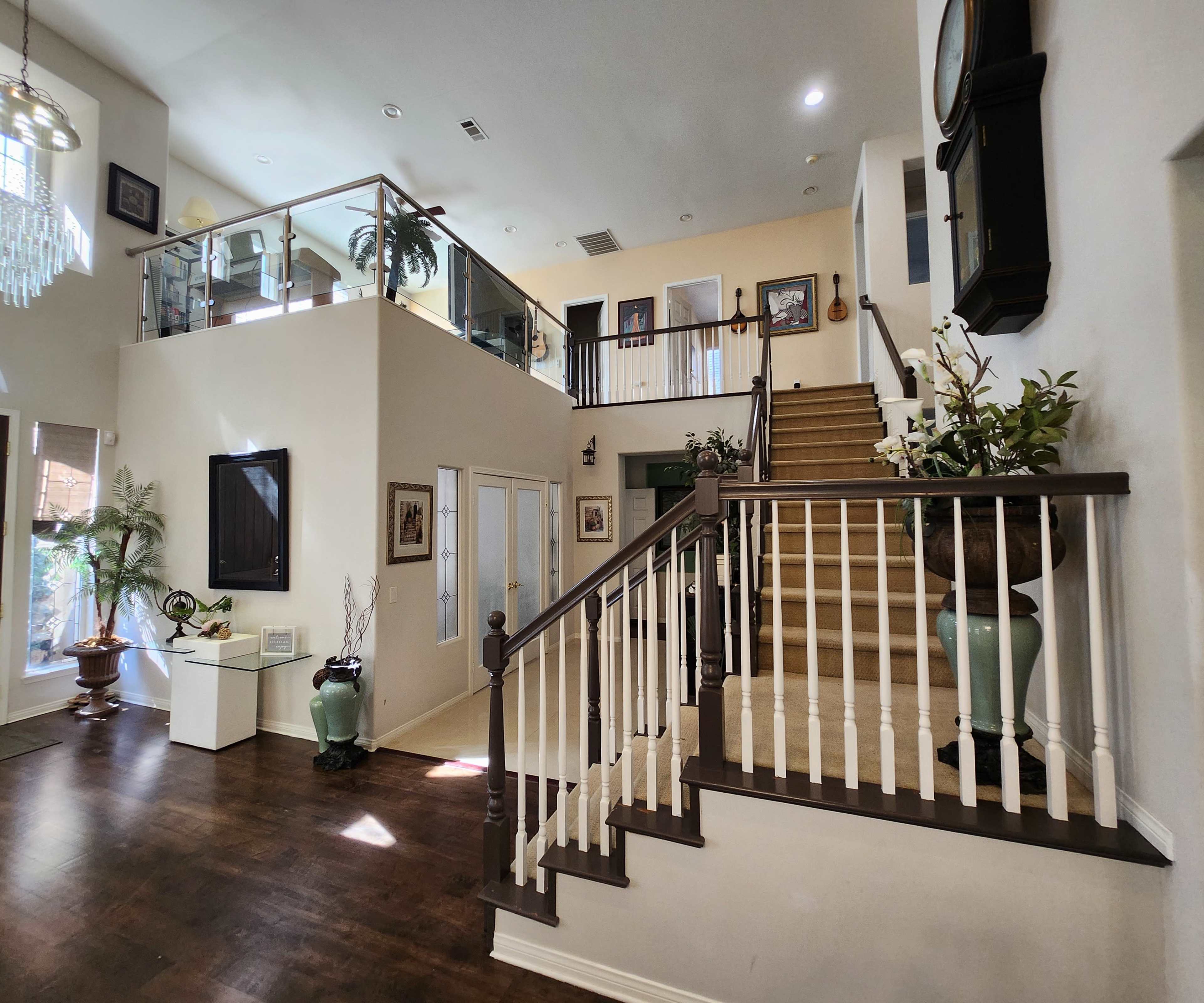A spacious foyer features a staircase leading to a second level, with a glass railing and various plants arranged throughout the area.