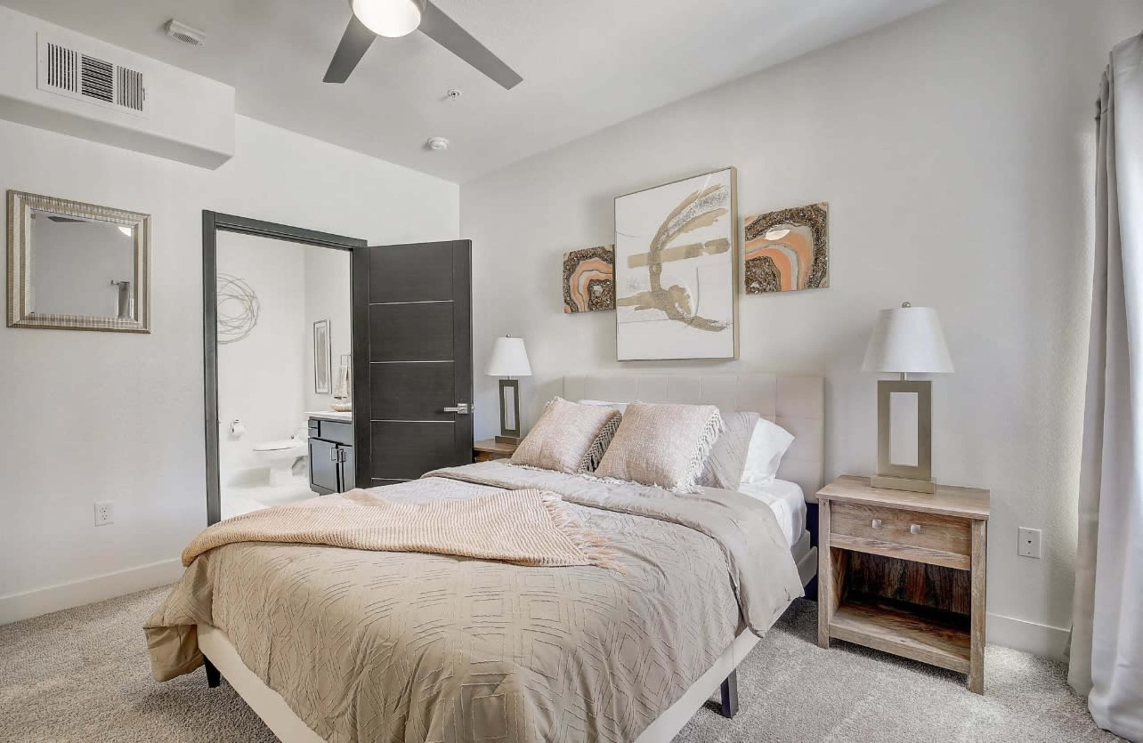 A modern bedroom featuring a bed with a light-colored comforter, bedside tables with lamps, and abstract artwork on the wall.
