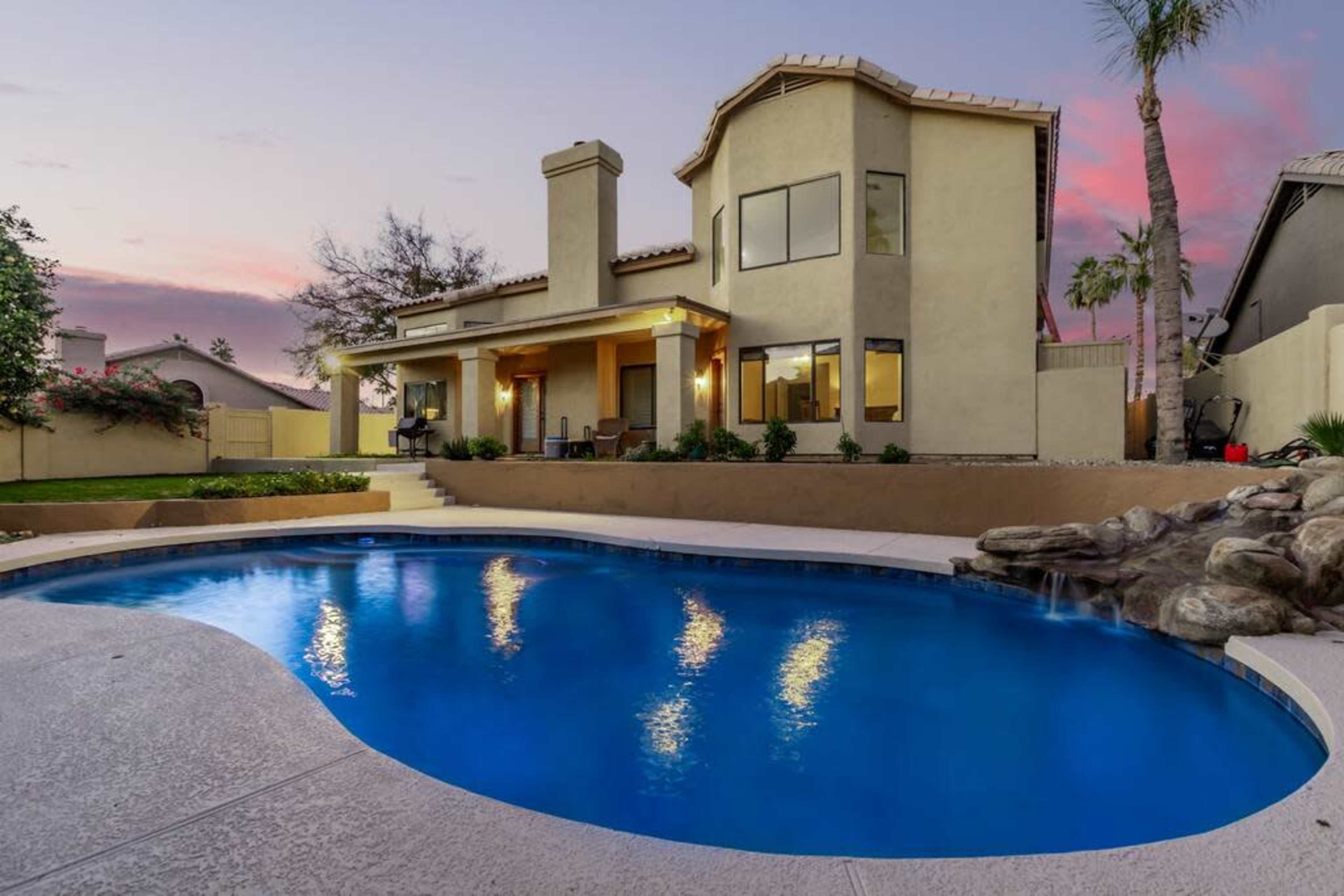 A modern house with a swimming pool in the backyard is illuminated by the evening sky.