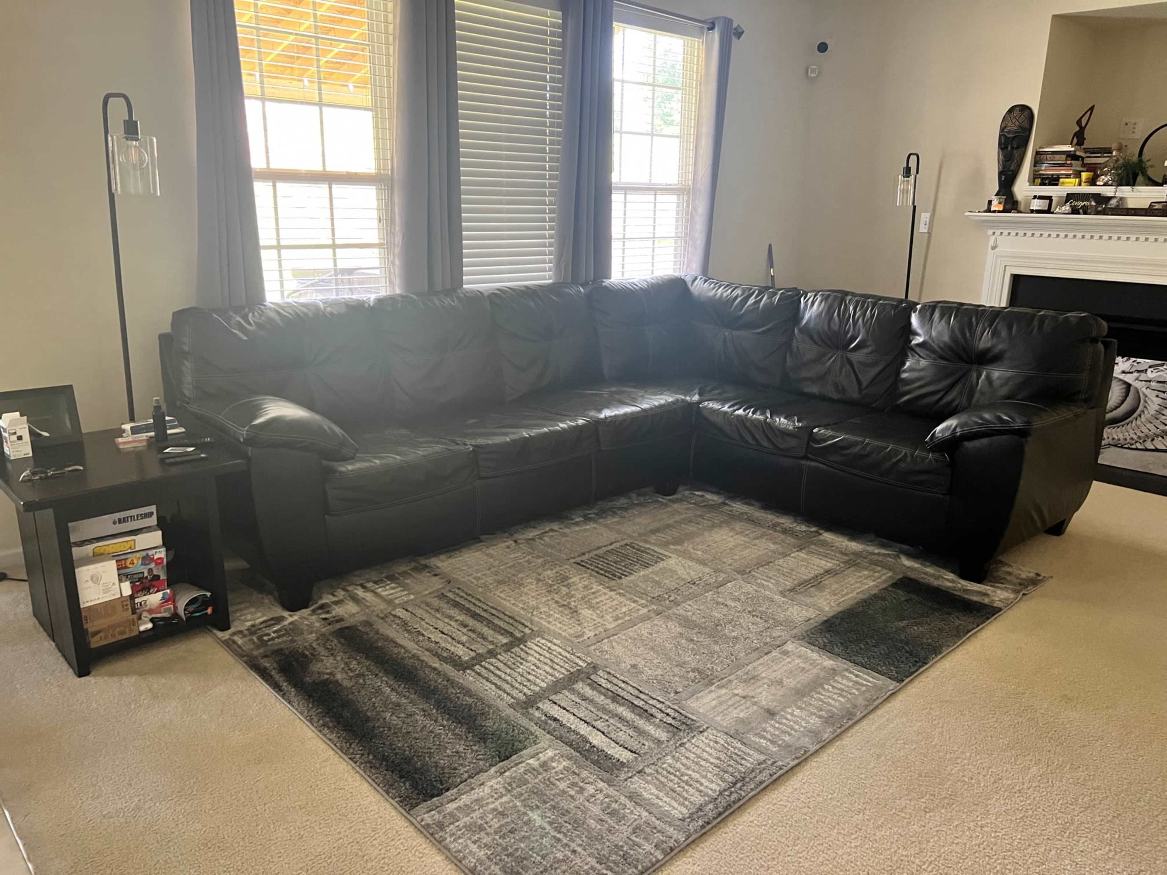 A black leather sectional sofa positioned in a living room with a light-colored carpet and a coffee table beside it.
