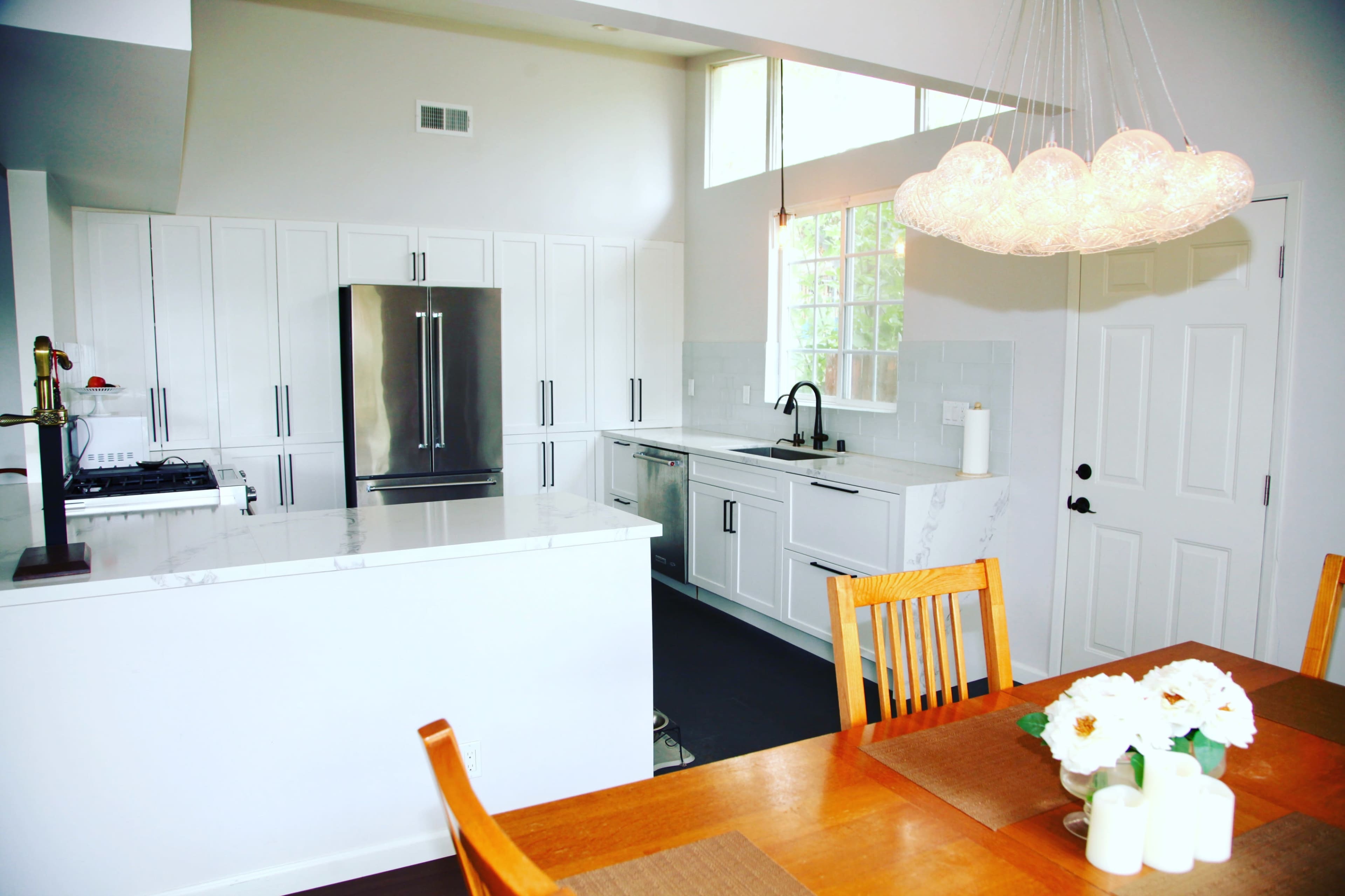 A modern kitchen features white cabinetry, stainless steel appliances, and a dining table with a vase of flowers.