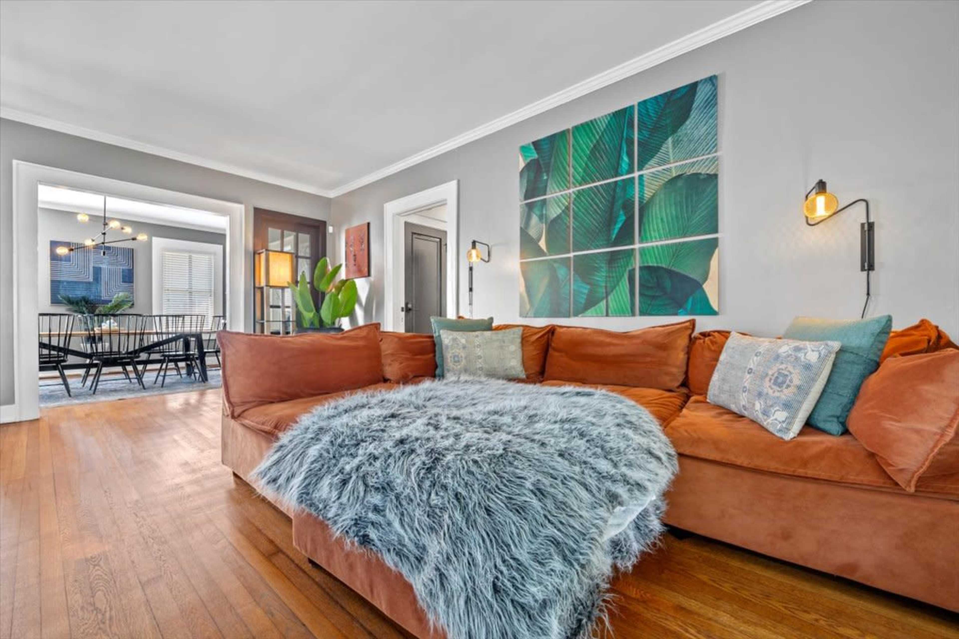 A cozy living room features a large brown sectional sofa adorned with a soft throw blanket and decorative pillows, with a view into a dining area beyond.