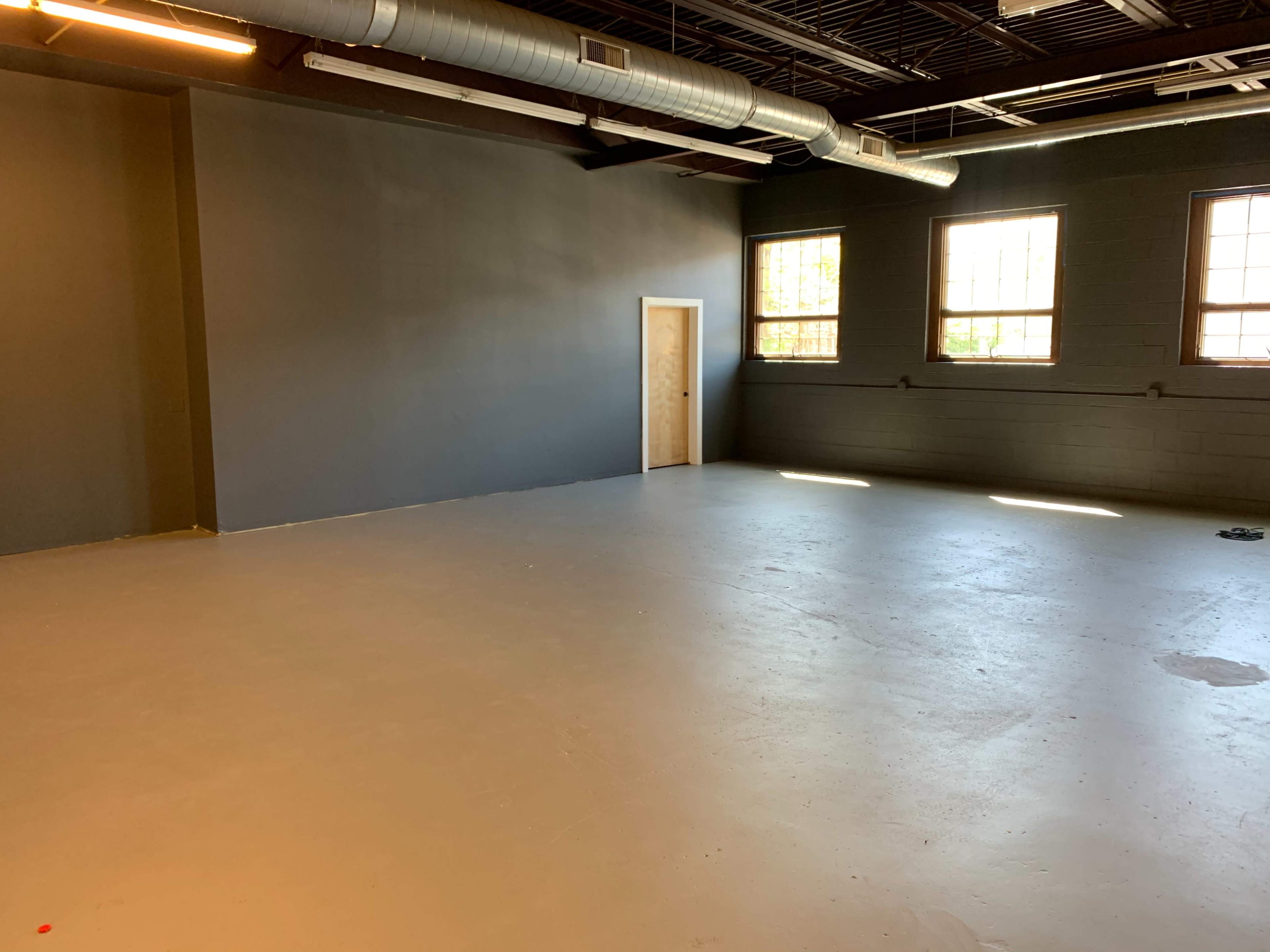 An empty room with gray walls, large windows, and a single door.