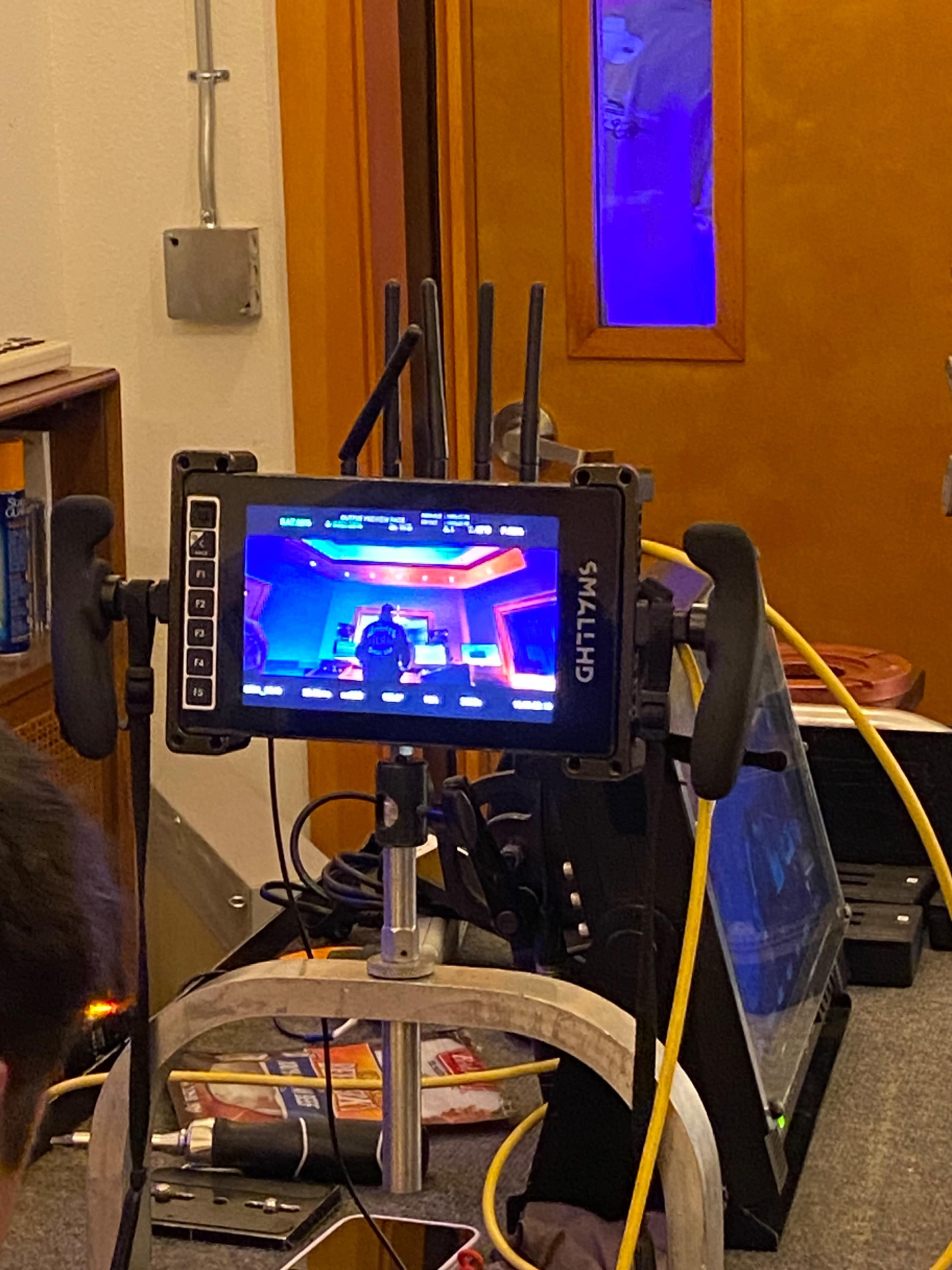 A camera monitor displays a brightly lit futuristic set, surrounded by various pieces of filming equipment.