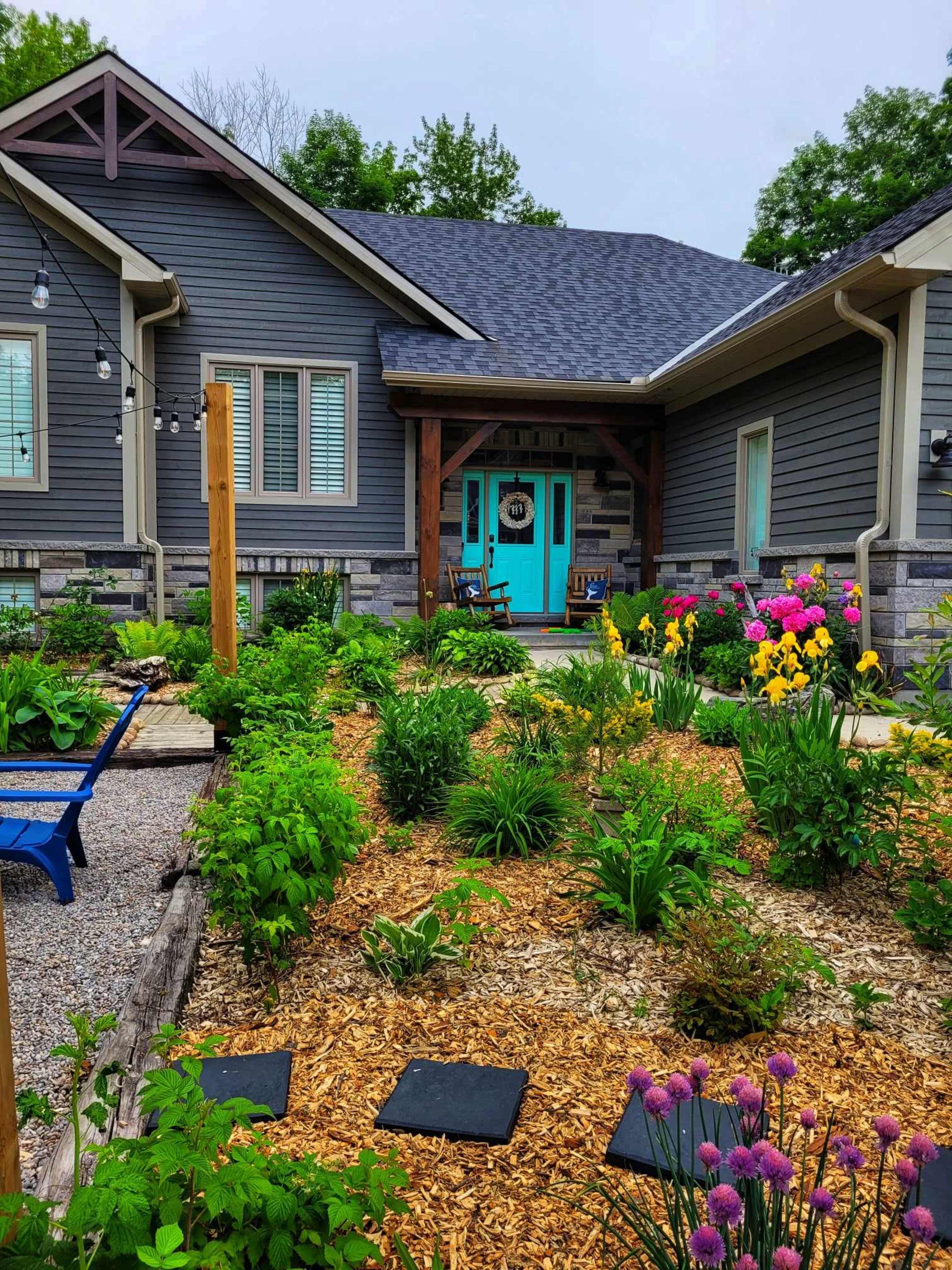 A well-maintained garden with colorful flowers and greenery surrounds a modern home featuring a blue front door.