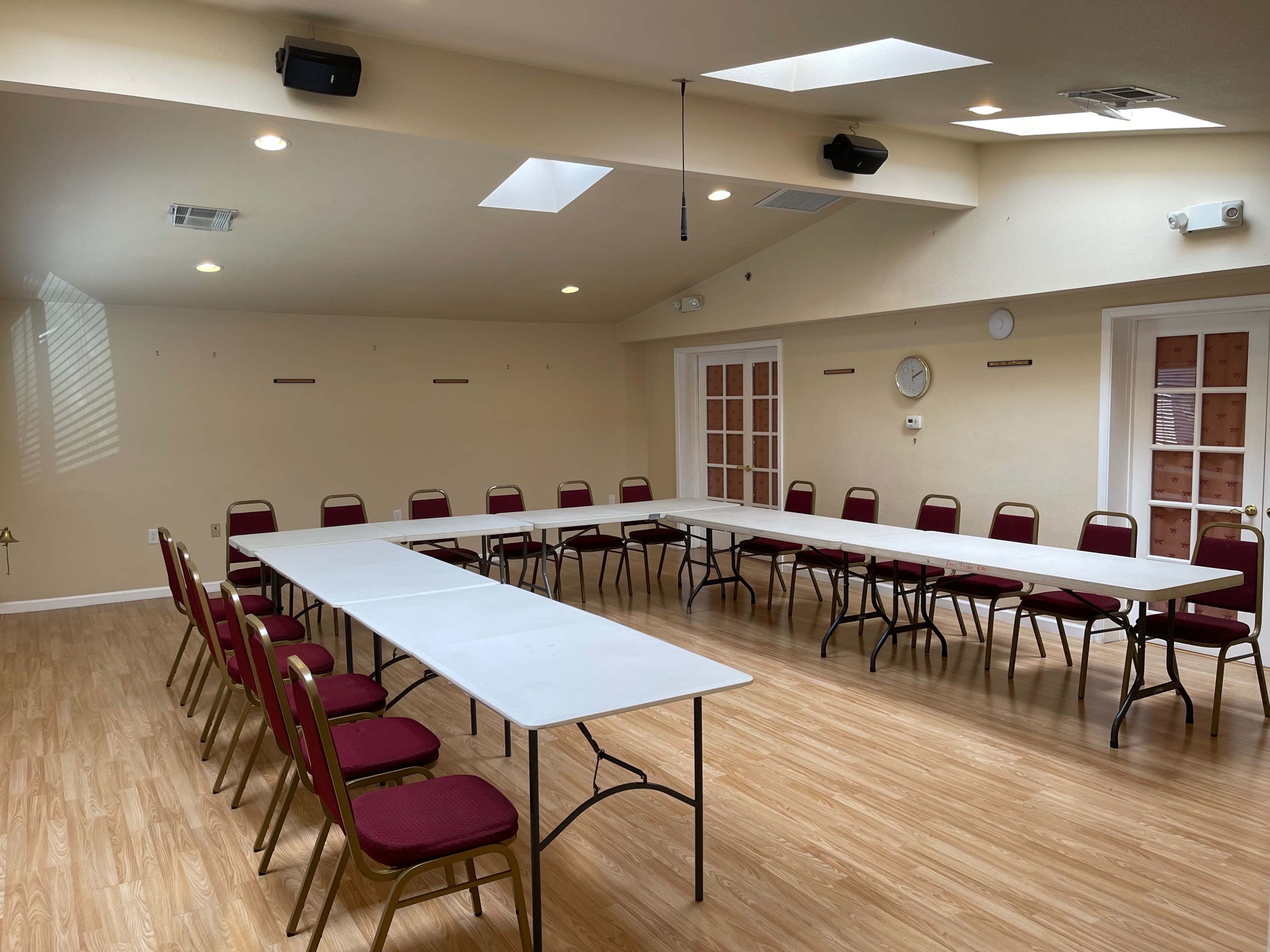 A meeting room with a set of tables arranged in a U-shape, surrounded by chairs along the perimeter.