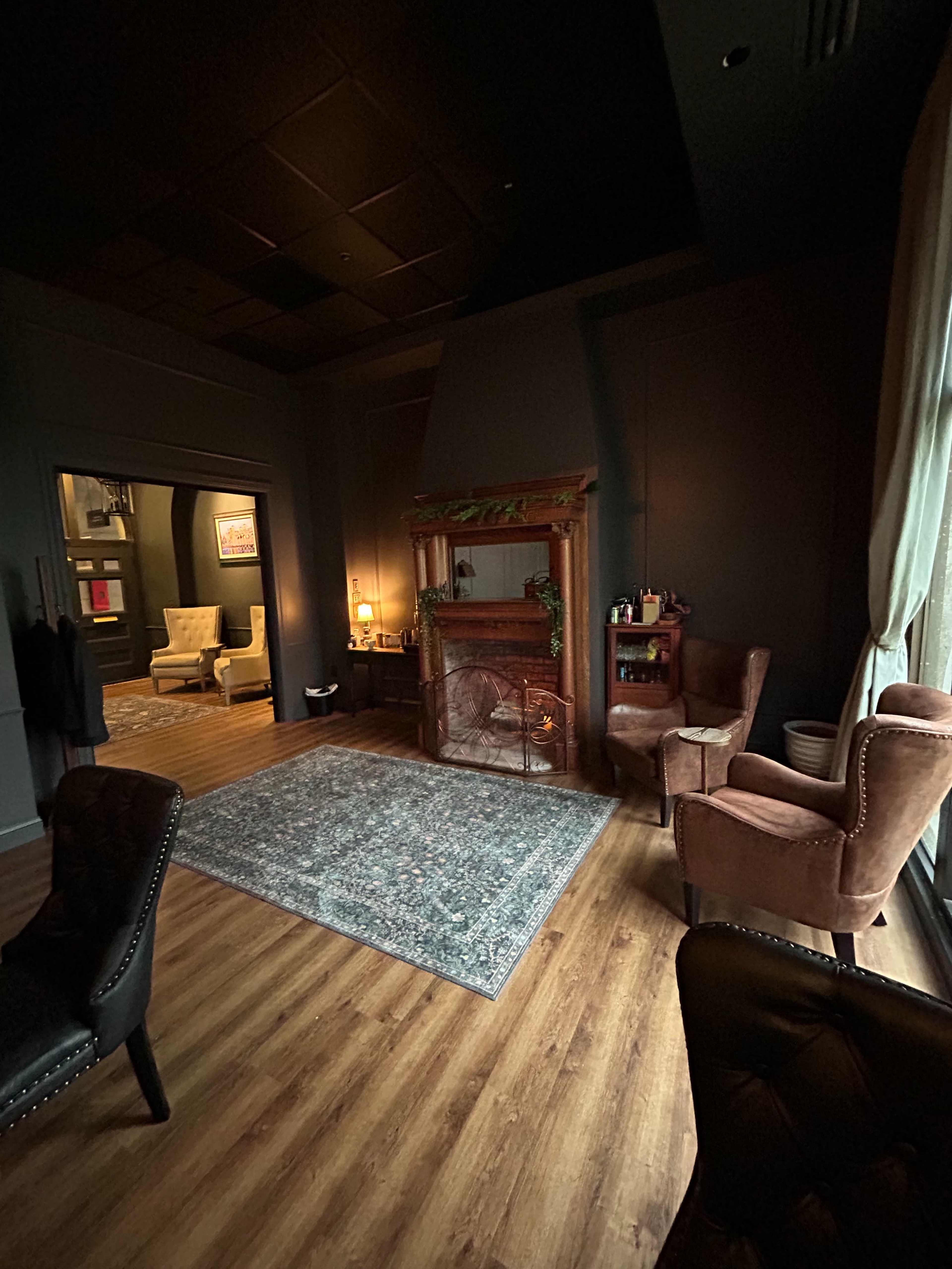 The image shows a cozy room featuring a fireplace, two armchairs, a rug, and a doorway leading to another space.