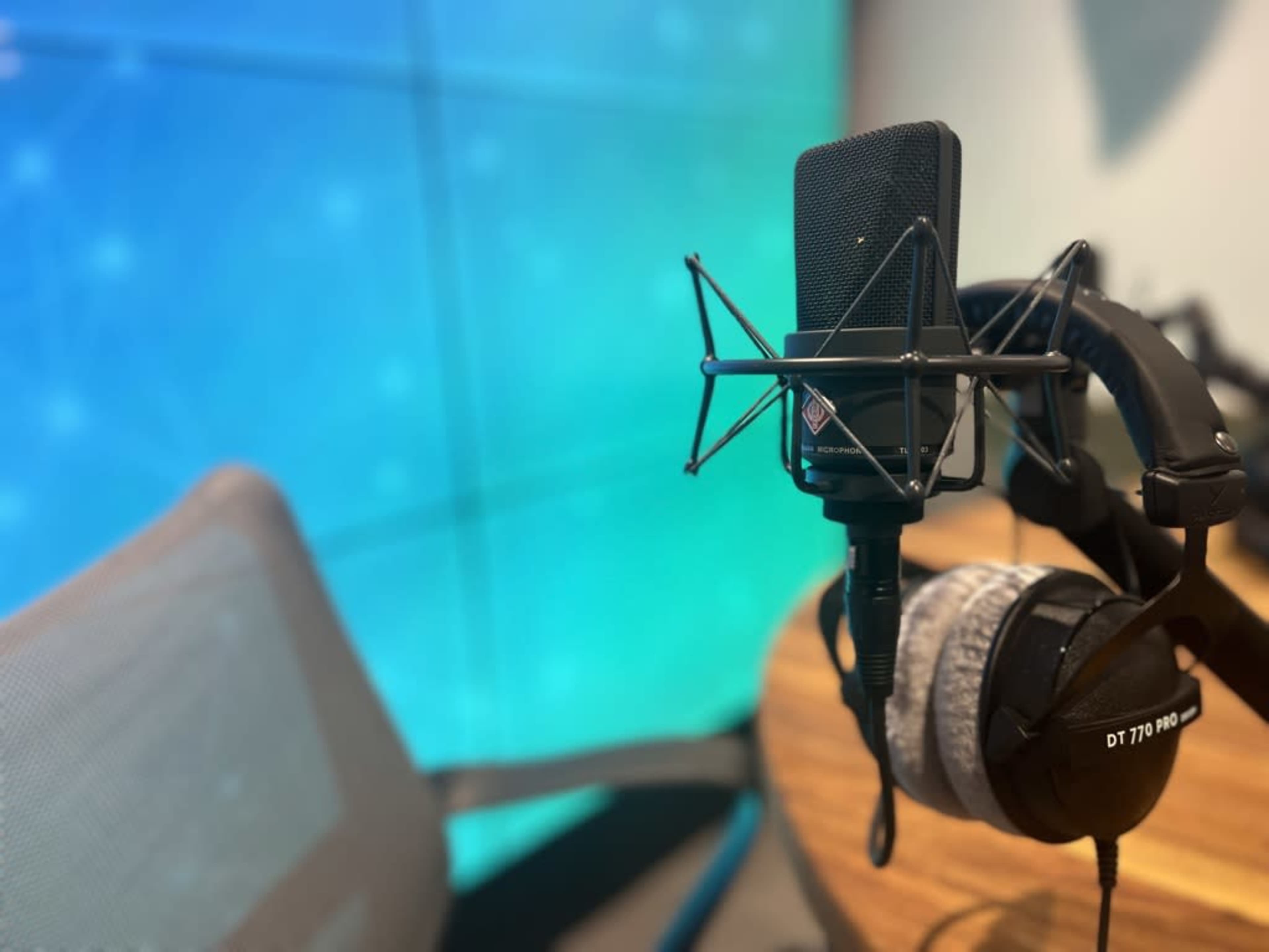 A microphone is mounted on a stand next to a pair of headphones on a wooden table in a recording studio.