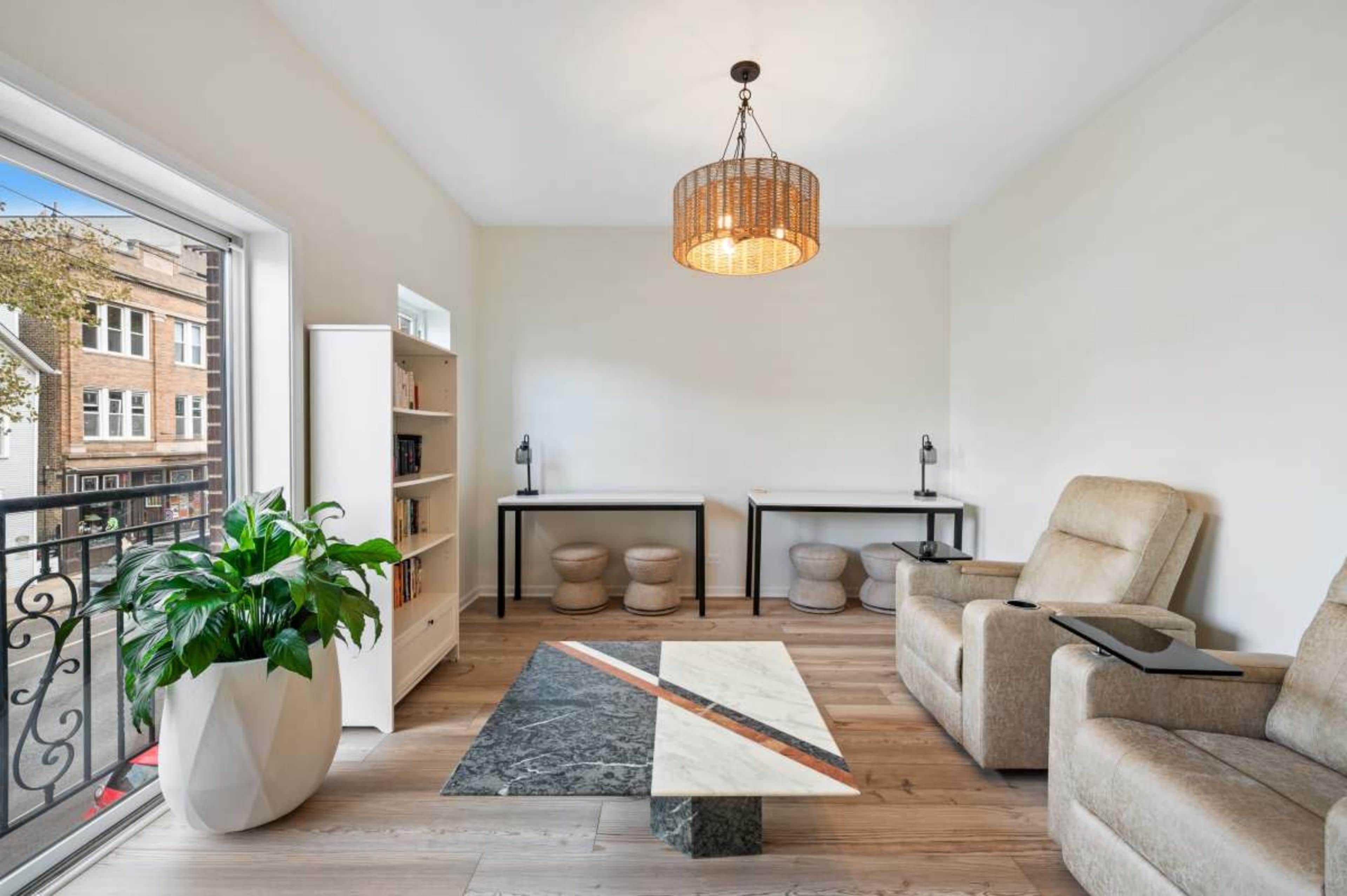 The image shows a modern living room with two armchairs, a geometric coffee table, and large windows letting in natural light.
