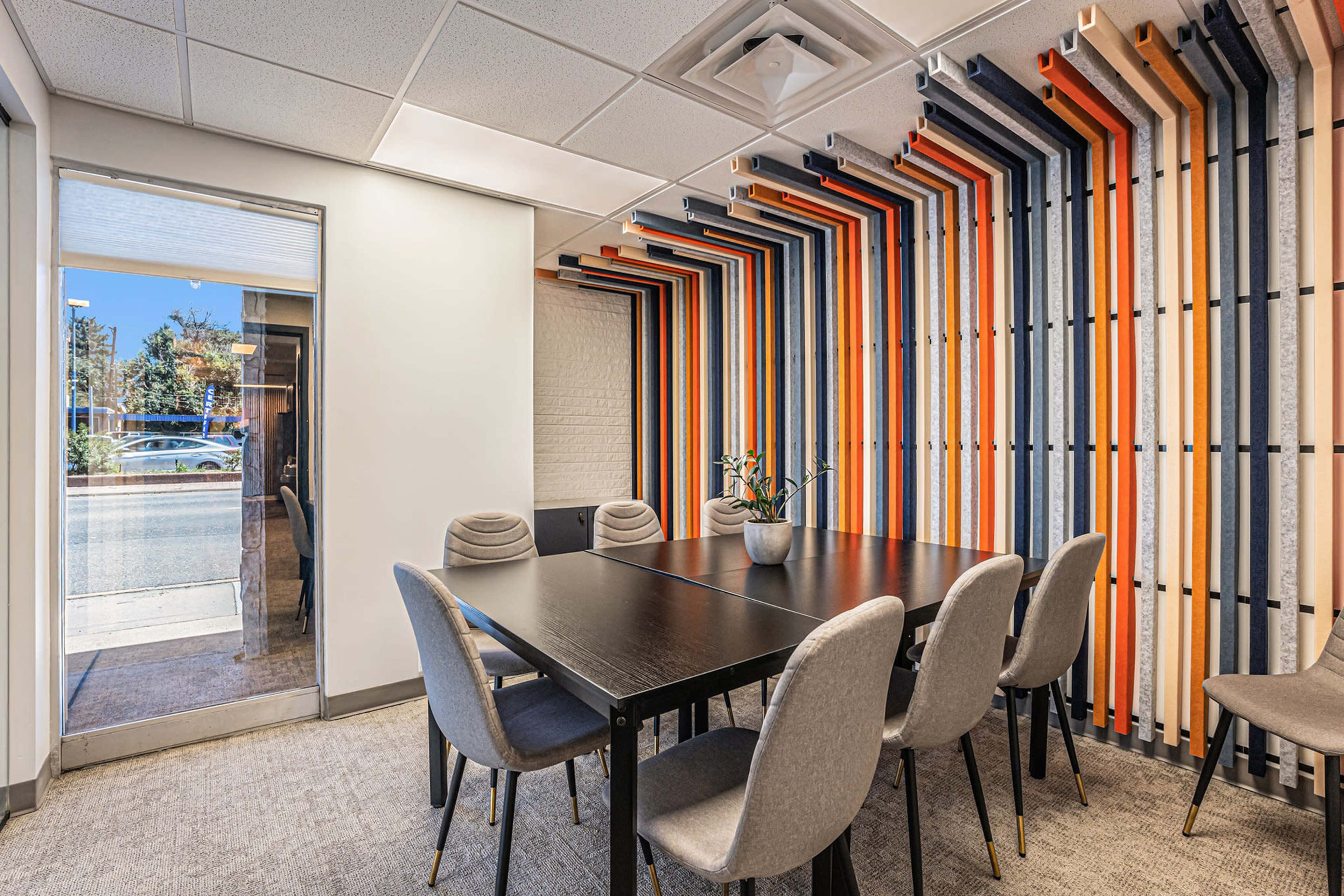 A conference room features a black table surrounded by six gray chairs and a colorful striped accent wall.