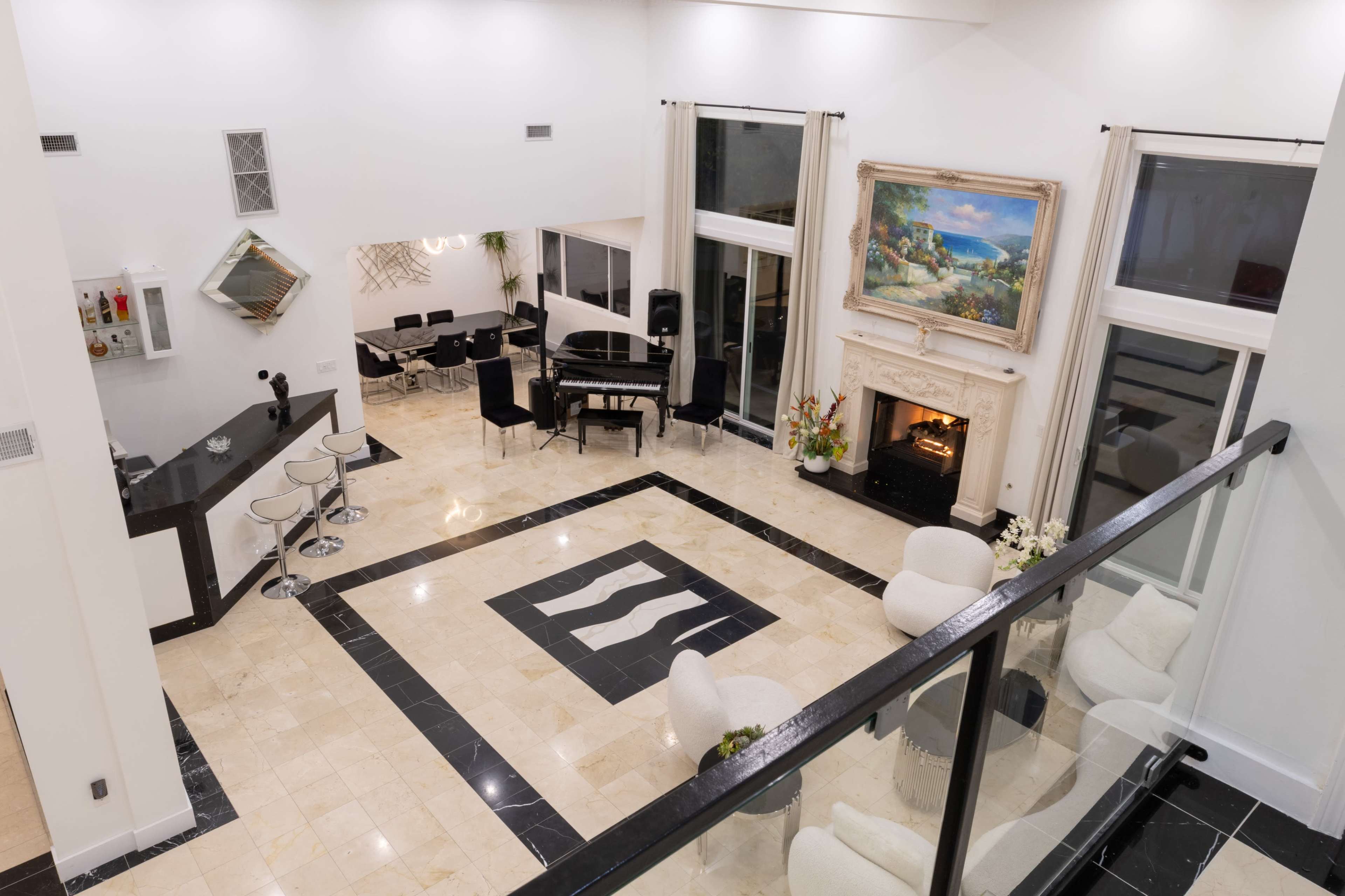 The image shows a spacious, modern living room with a grand piano, a fireplace, and a large painting, surrounded by elegant furniture.