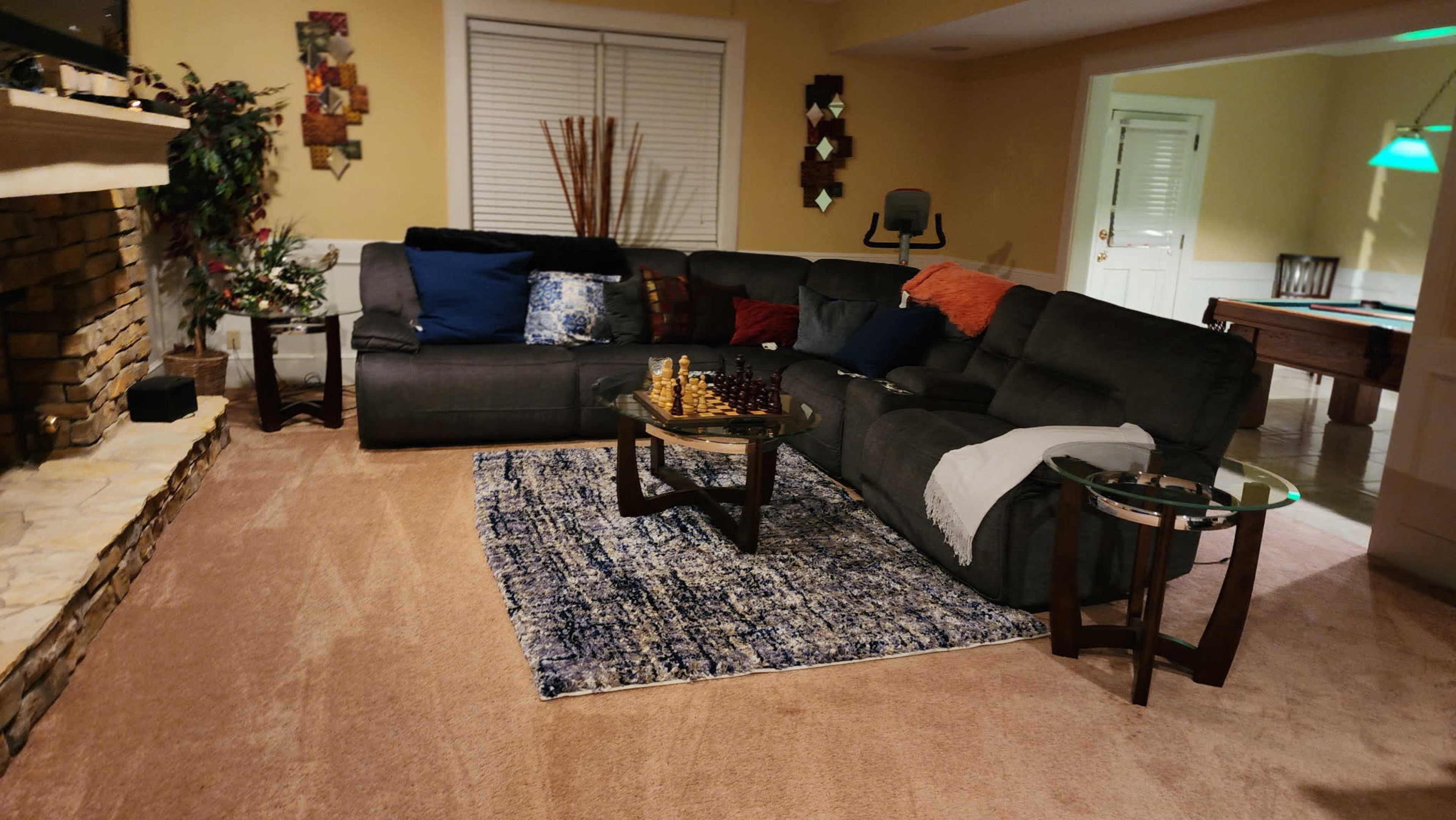 The image shows a living room featuring a dark gray sectional sofa, a patterned area rug, a coffee table, and a stone fireplace.