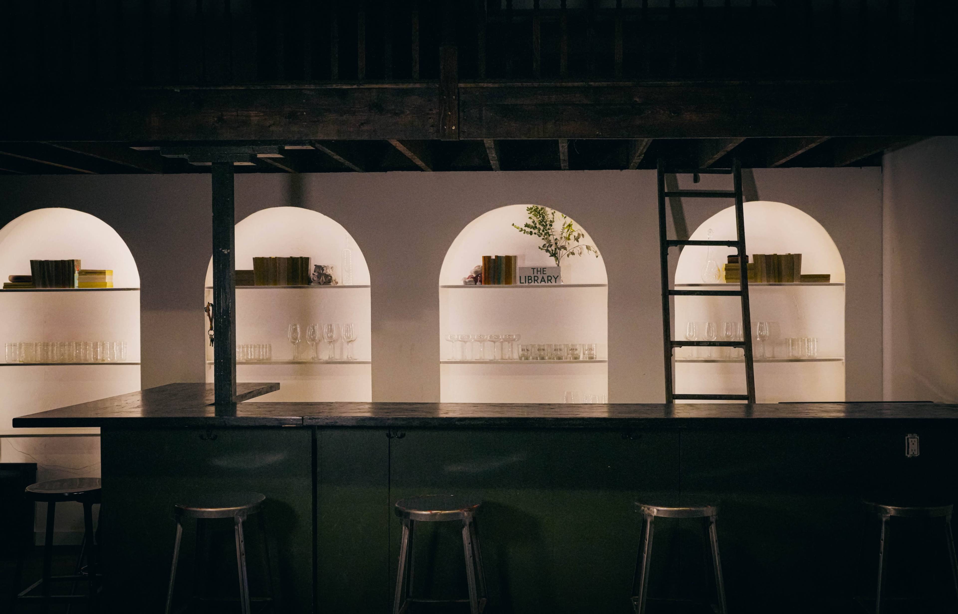 The image shows a dimly lit bar area with a sleek counter and several arched recesses displaying various items on shelves.